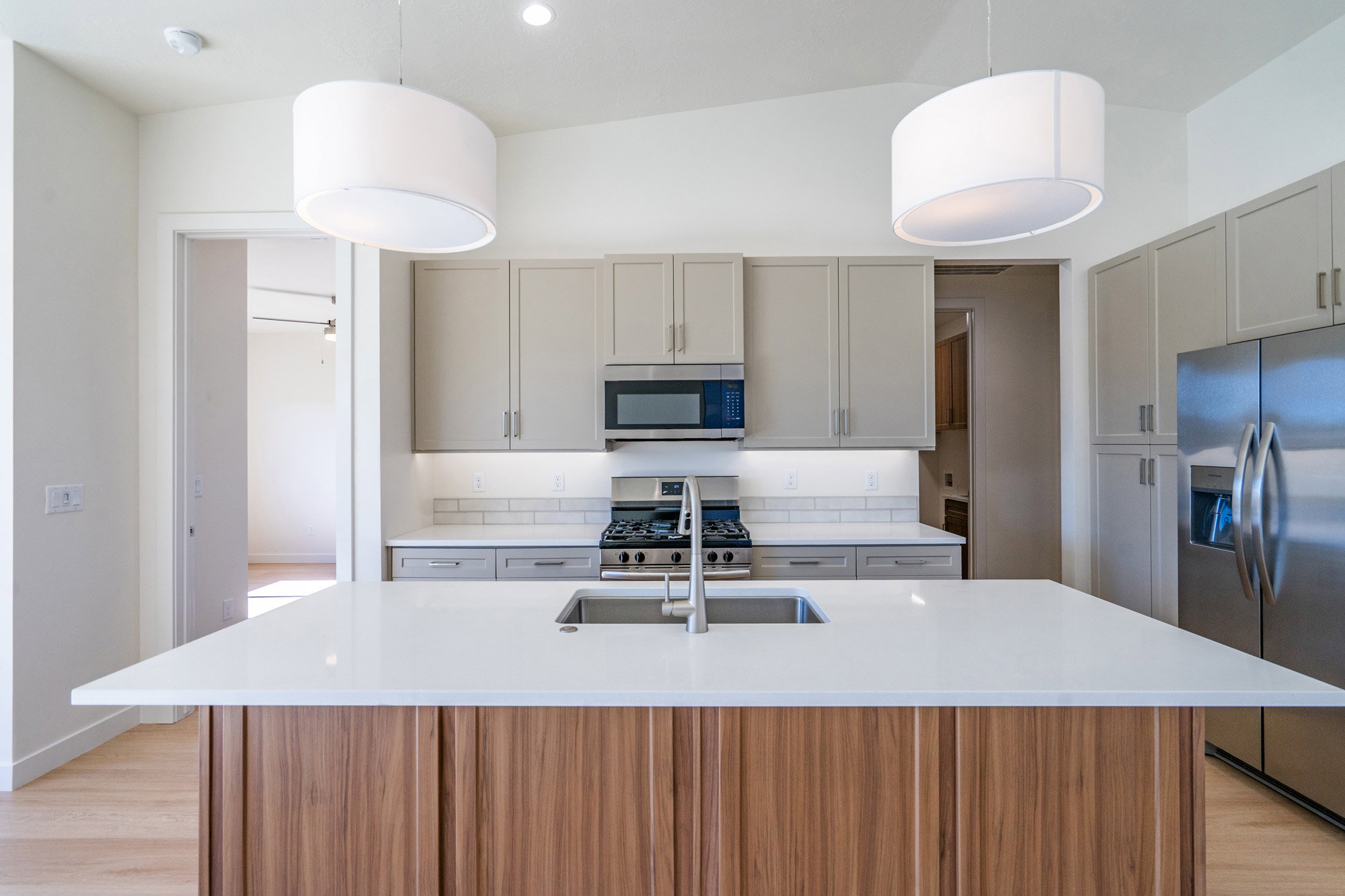 Kitchen featuring a center island with sink, stainless steel appliances, light wood-type flooring, and light stone countertops