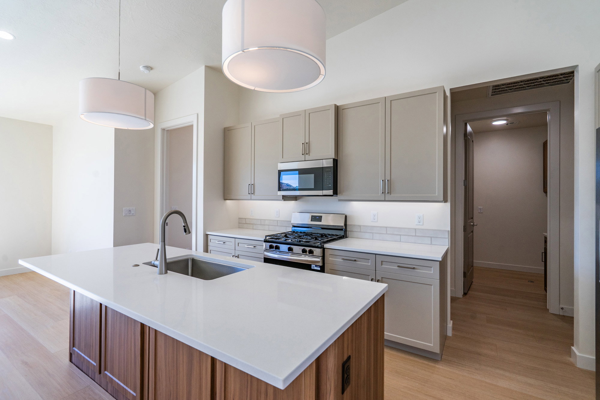 Kitchen with stainless steel appliances, a kitchen island with sink, light wood-style floors, light stone countertops, and two tone cabinetry