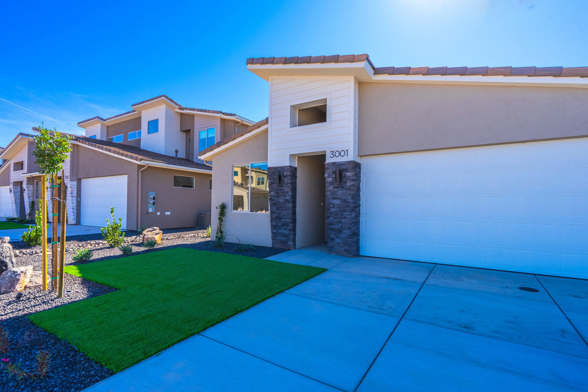 Contemporary home with stucco siding, a front yard, an attached garage, concrete driveway, and stone siding