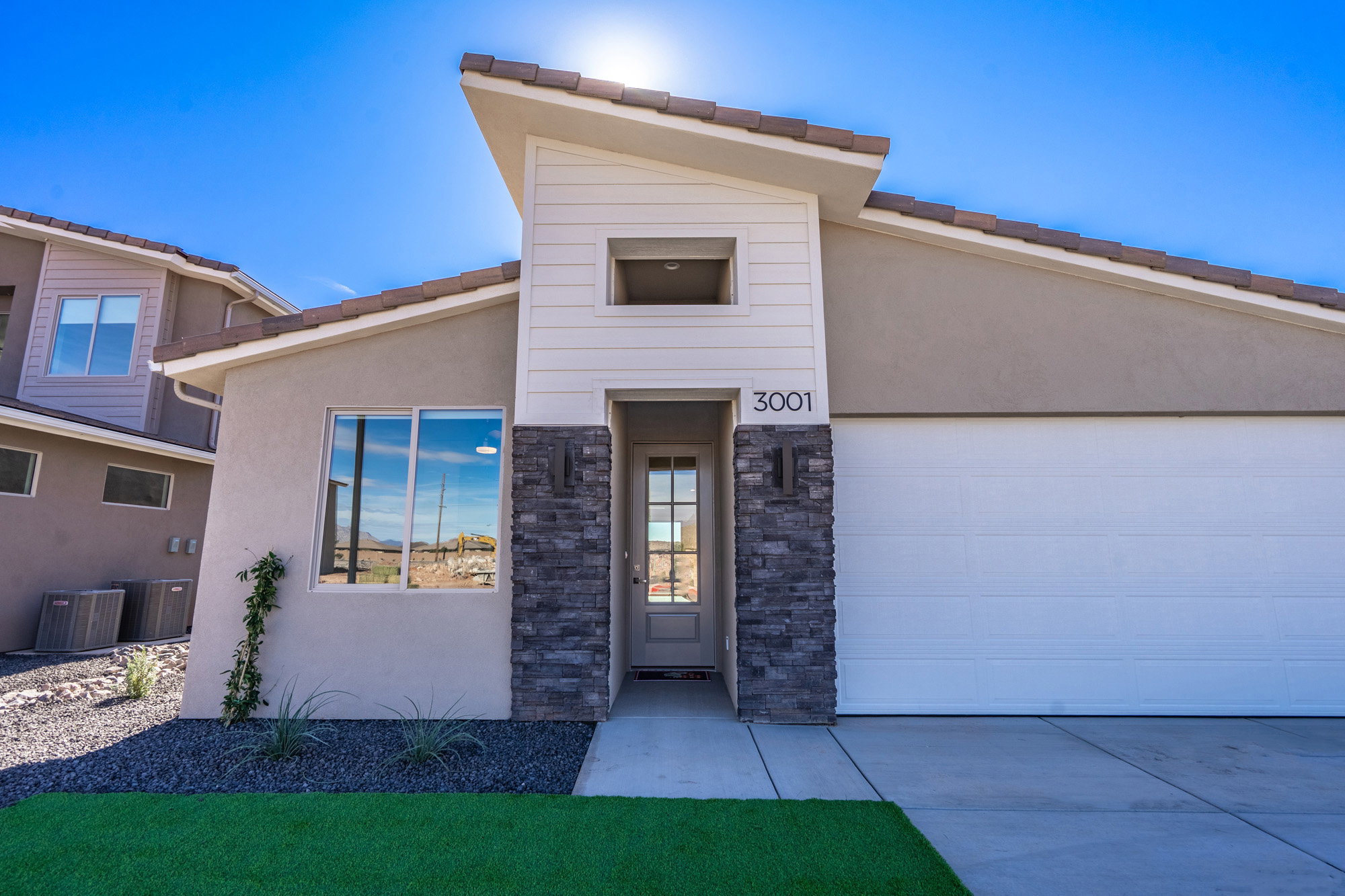 View of front of home with stucco siding, stone siding, an attached garage, driveway, and a tiled roof