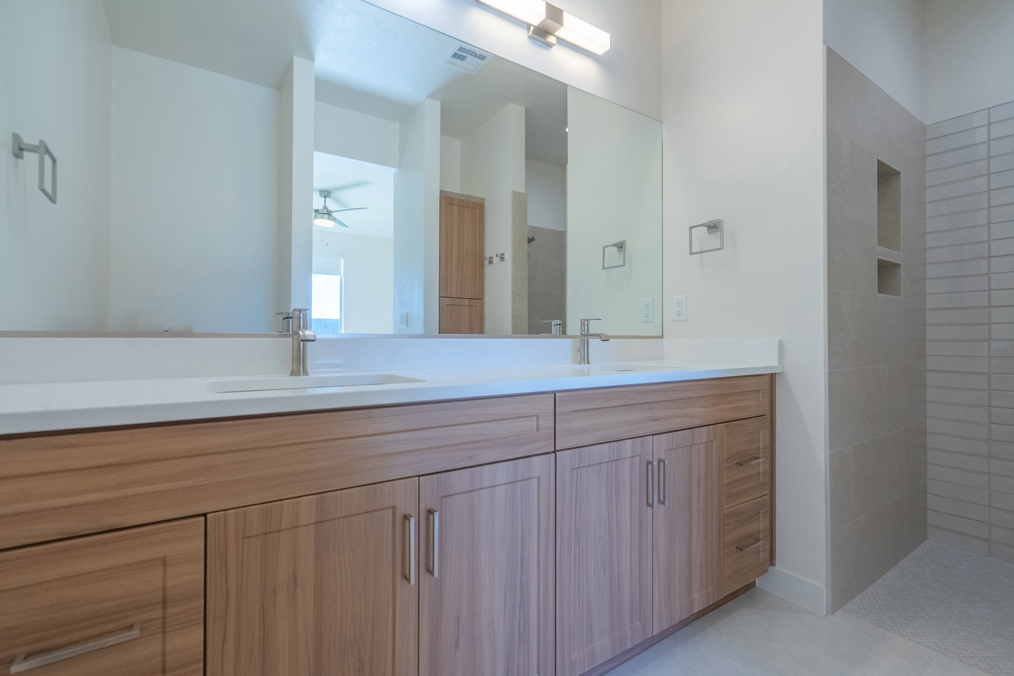 Bathroom with double vanity, ceiling fan, and tiled shower