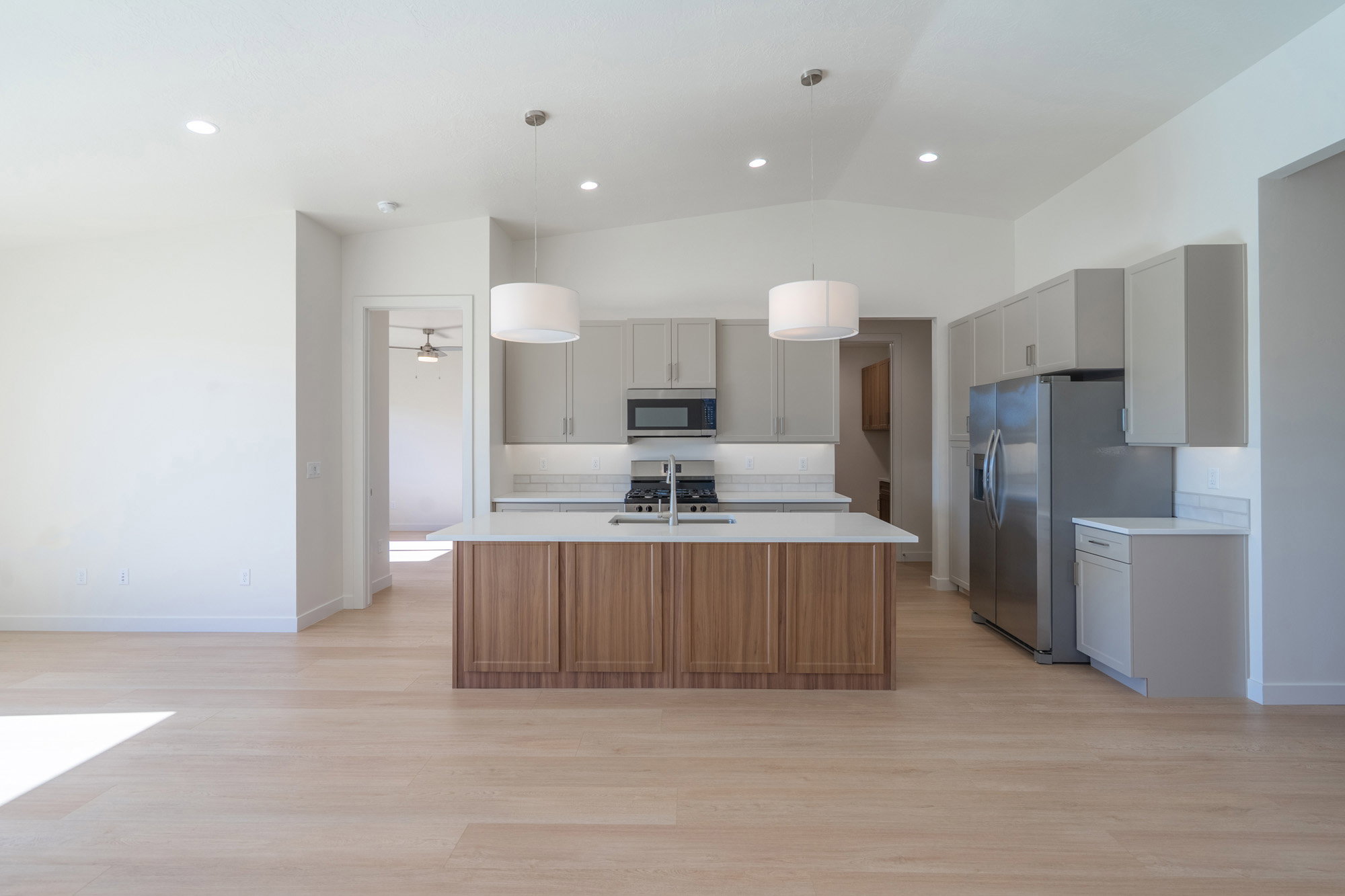 Dual tone kitchen with a center island with sink, light wood-type flooring, decorative light fixtures, vaulted ceiling, and stainless steel appliances