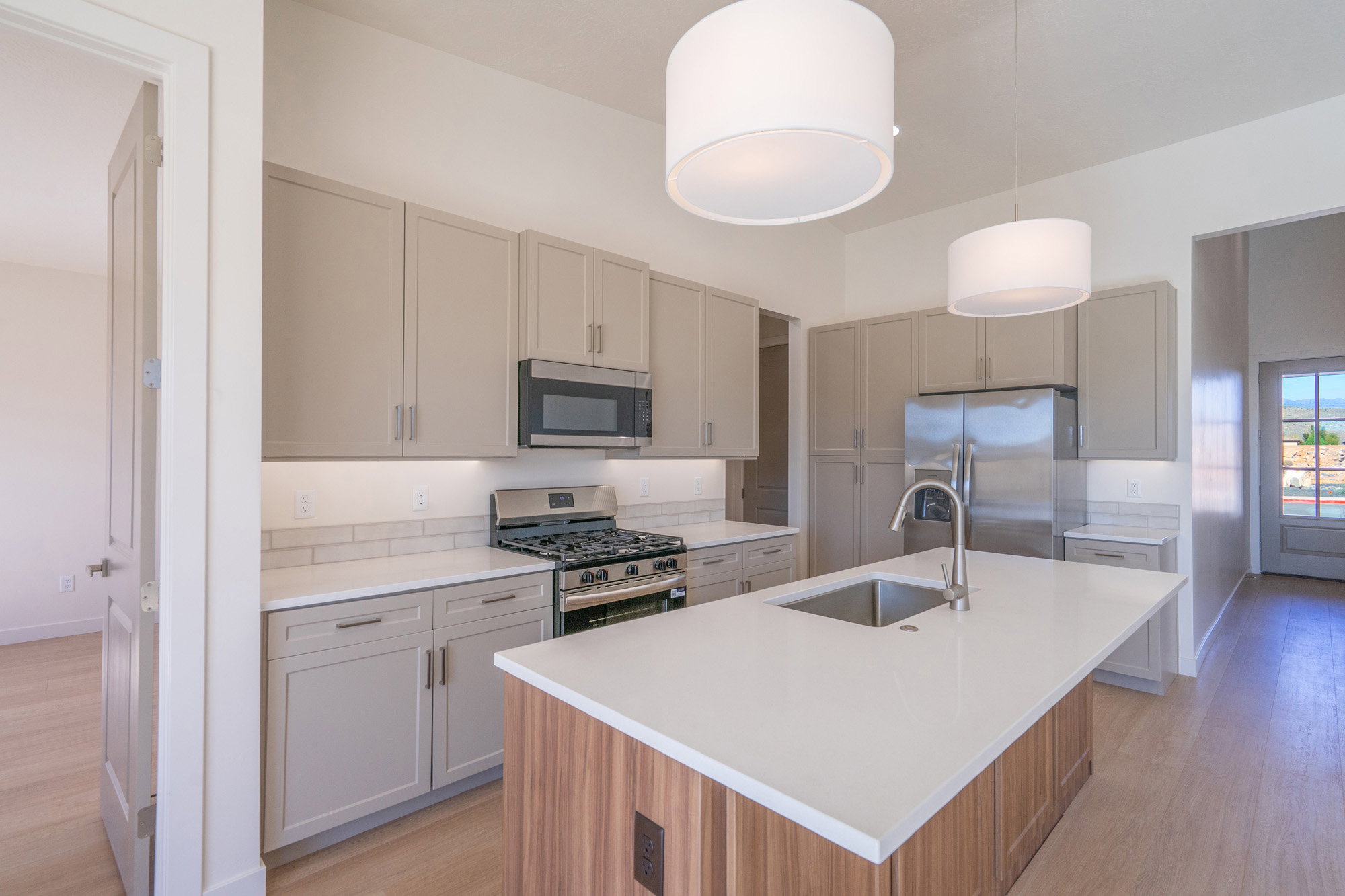 Kitchen featuring stainless steel appliances, a kitchen island with sink, light wood-style flooring, dual tone cabinets, and light stone countertops