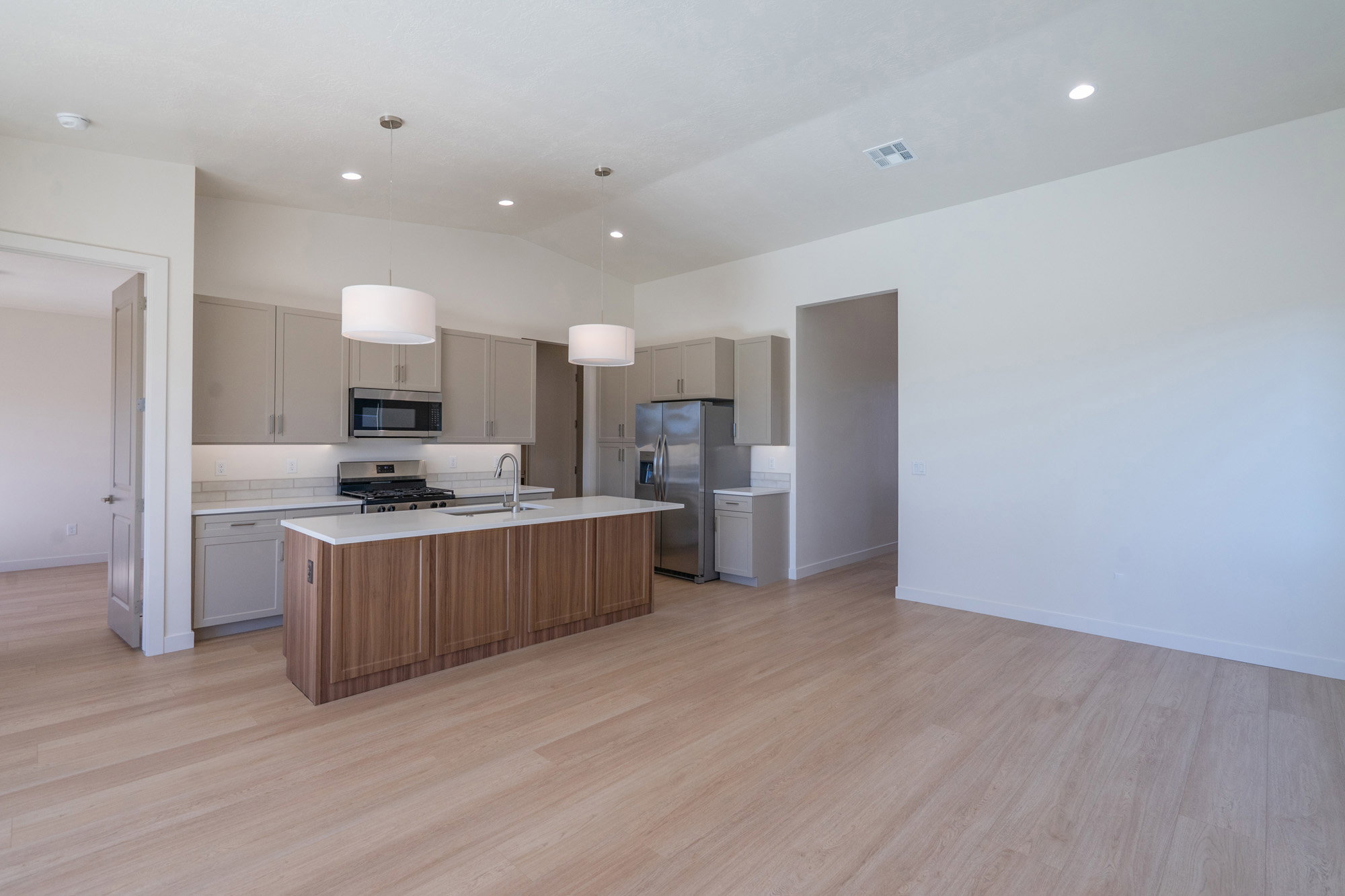 Kitchen with an island with sink, hanging light fixtures, stainless steel appliances, light wood-style flooring, and vaulted ceiling