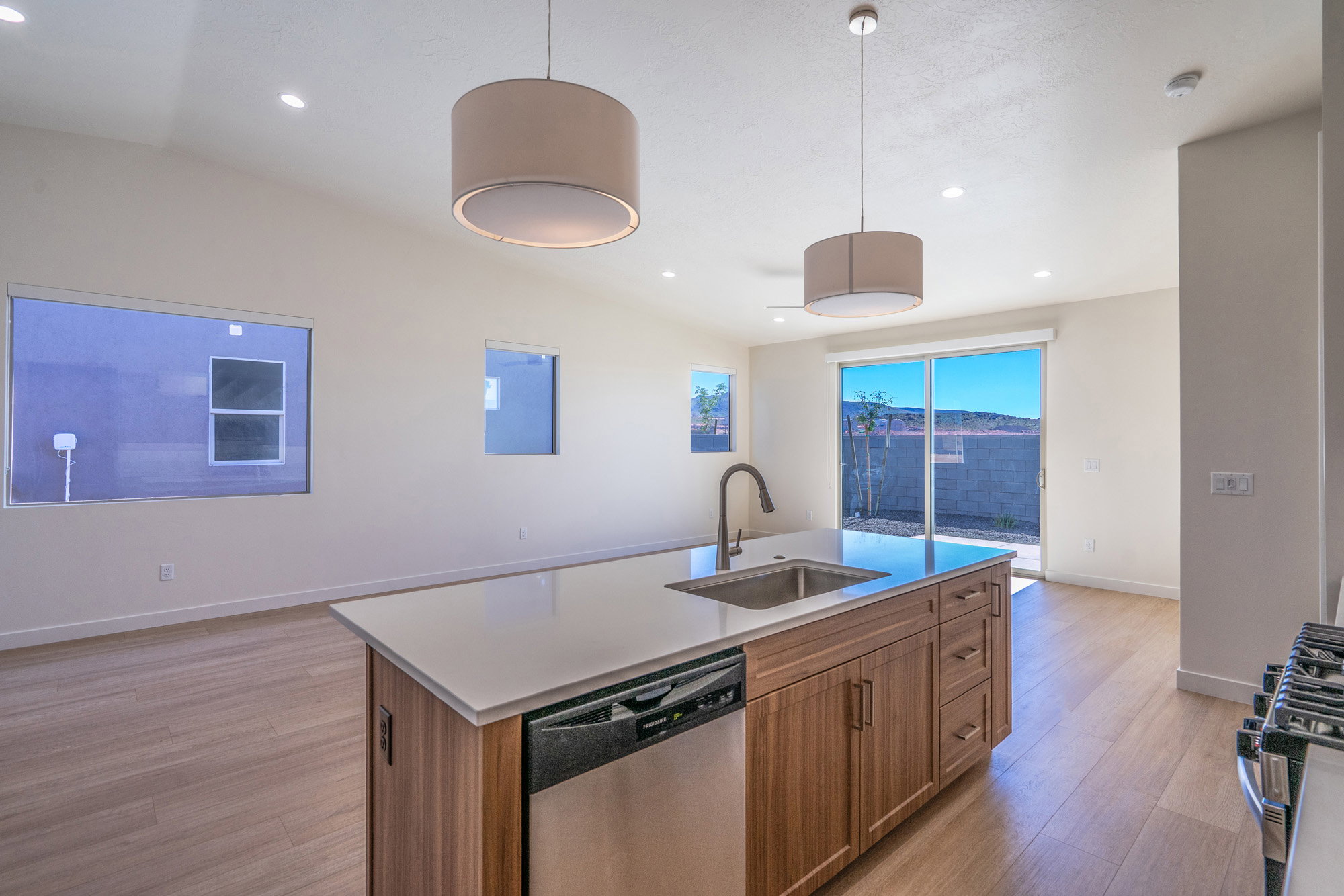 Kitchen featuring an island with sink, stainless steel appliances, light wood-style floors, decorative light fixtures, and lofted ceiling