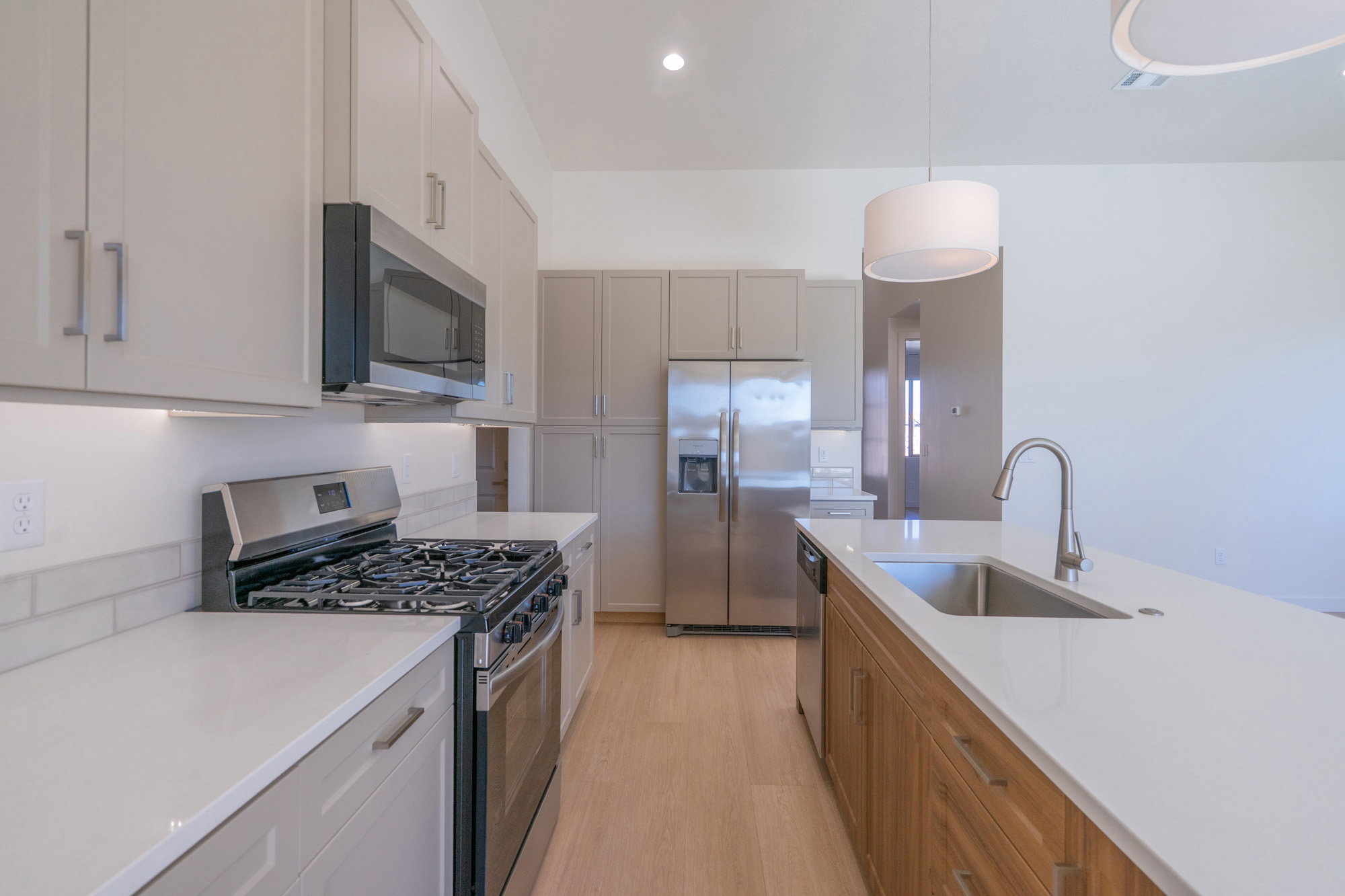 Dual tone kitchen with stainless steel appliances, light wood finished floors, decorative light fixtures, two tone cabinetry, and light stone counters