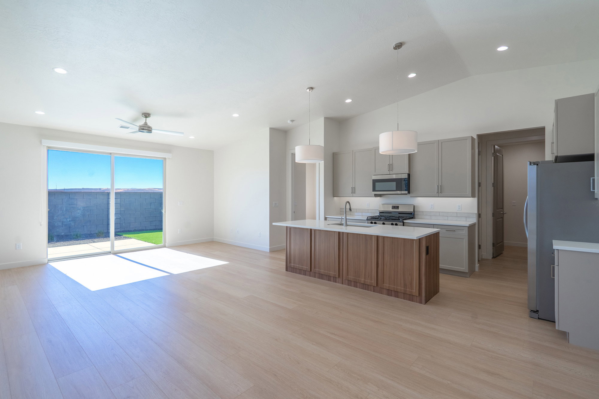 Two tone kitchen featuring stainless steel appliances, pendant lighting, a kitchen island with sink, open floor plan, and light wood-style flooring