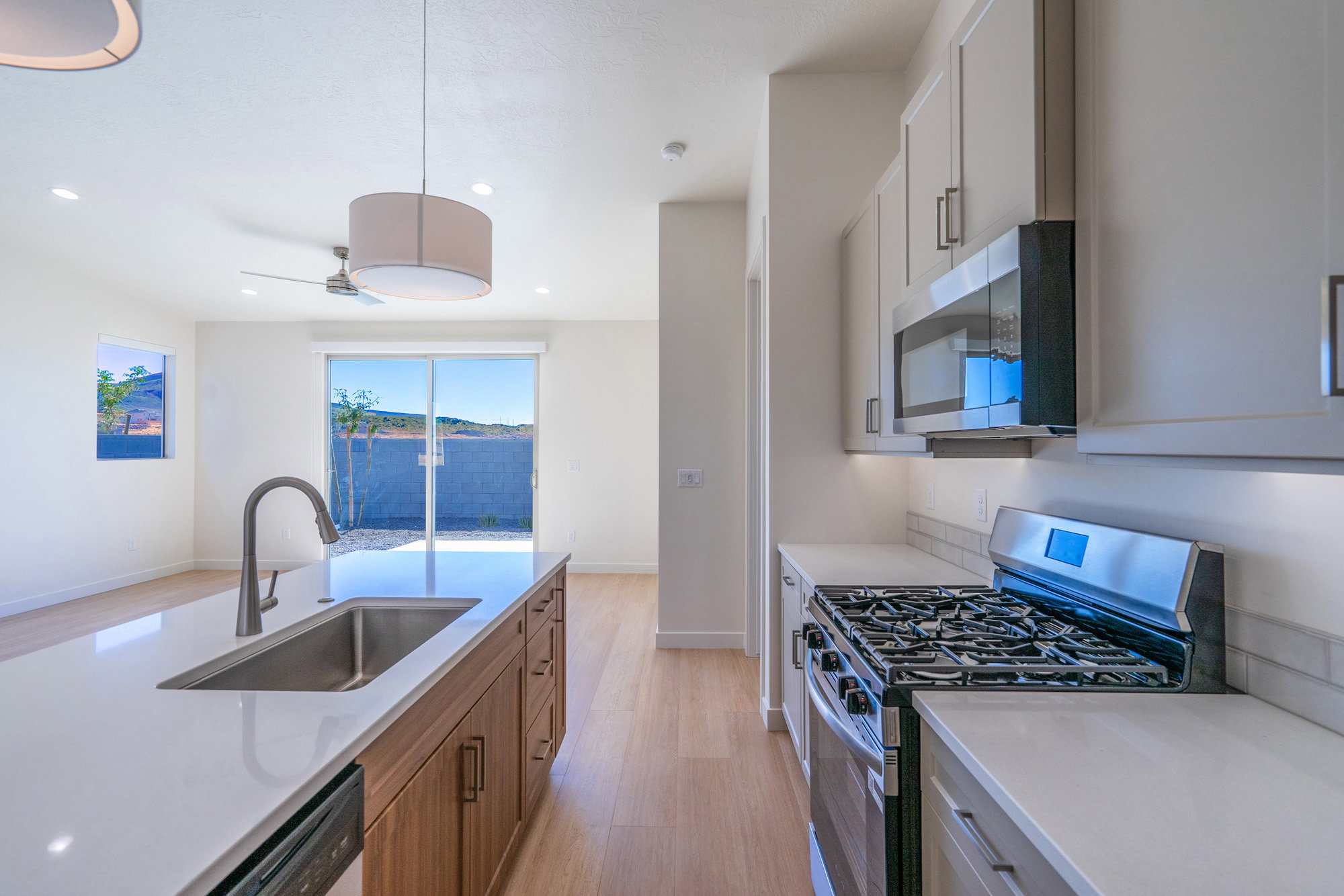Dual tone kitchen featuring stainless steel appliances, light wood-type flooring, light stone counters, two tone cabinetry, and a ceiling fan
