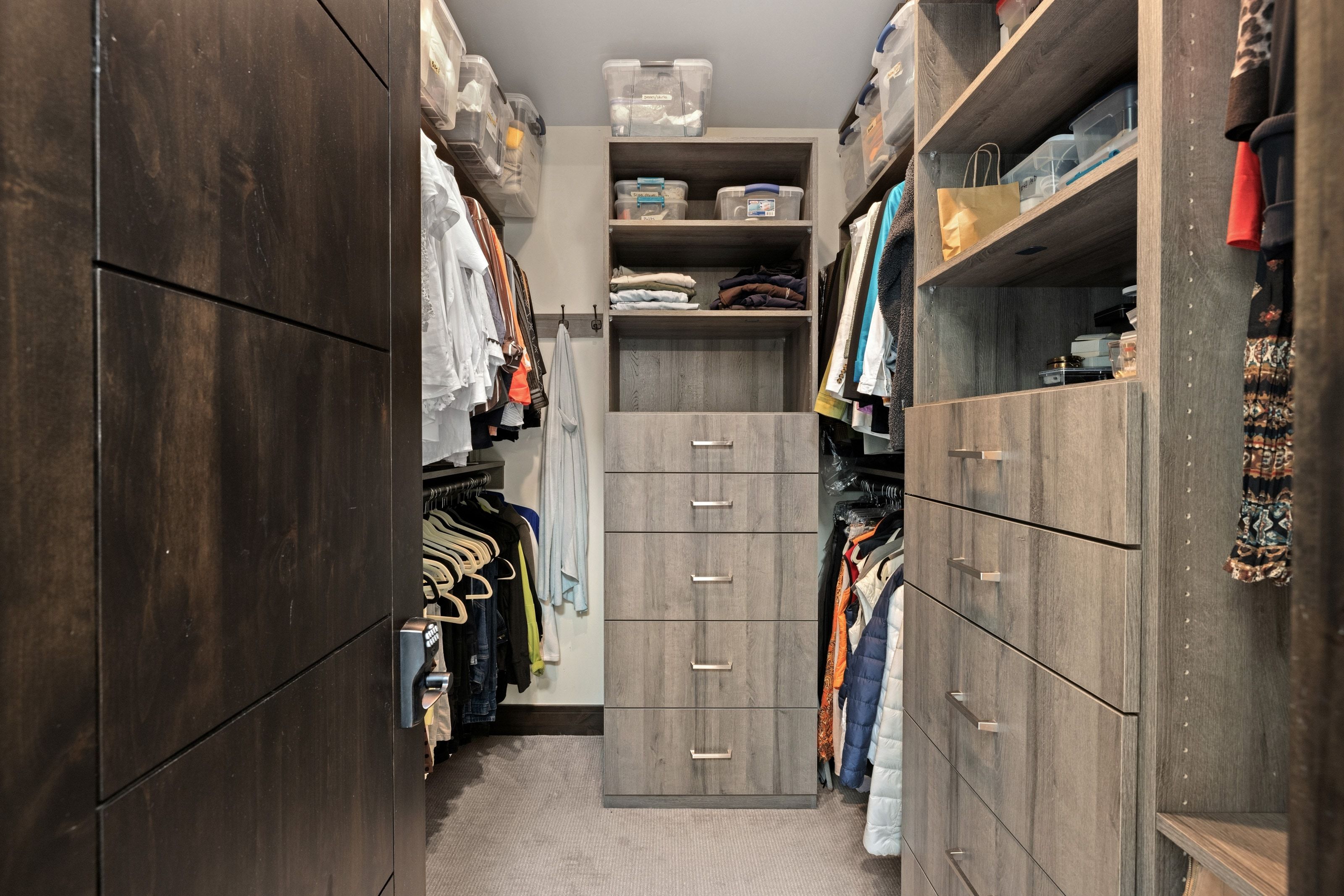 Custom closet system featuring dark wood-finish cabinetry, light wood-finish shelving, and integrated drawer storage with brushed metal pulls