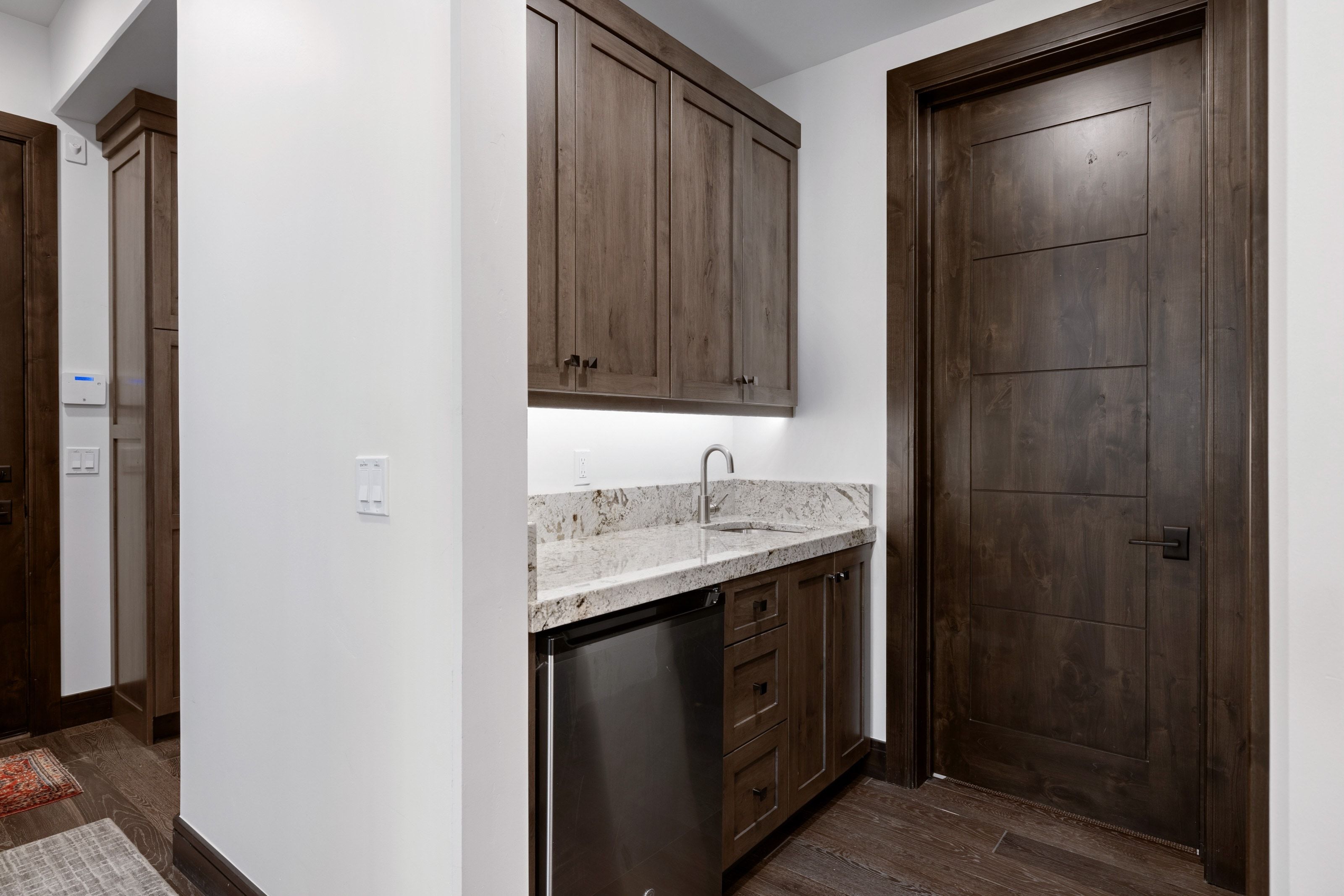 Wet bar featuring dark wood cabinetry, a light-toned granite countertop, and a stainless steel sink with a gooseneck faucet