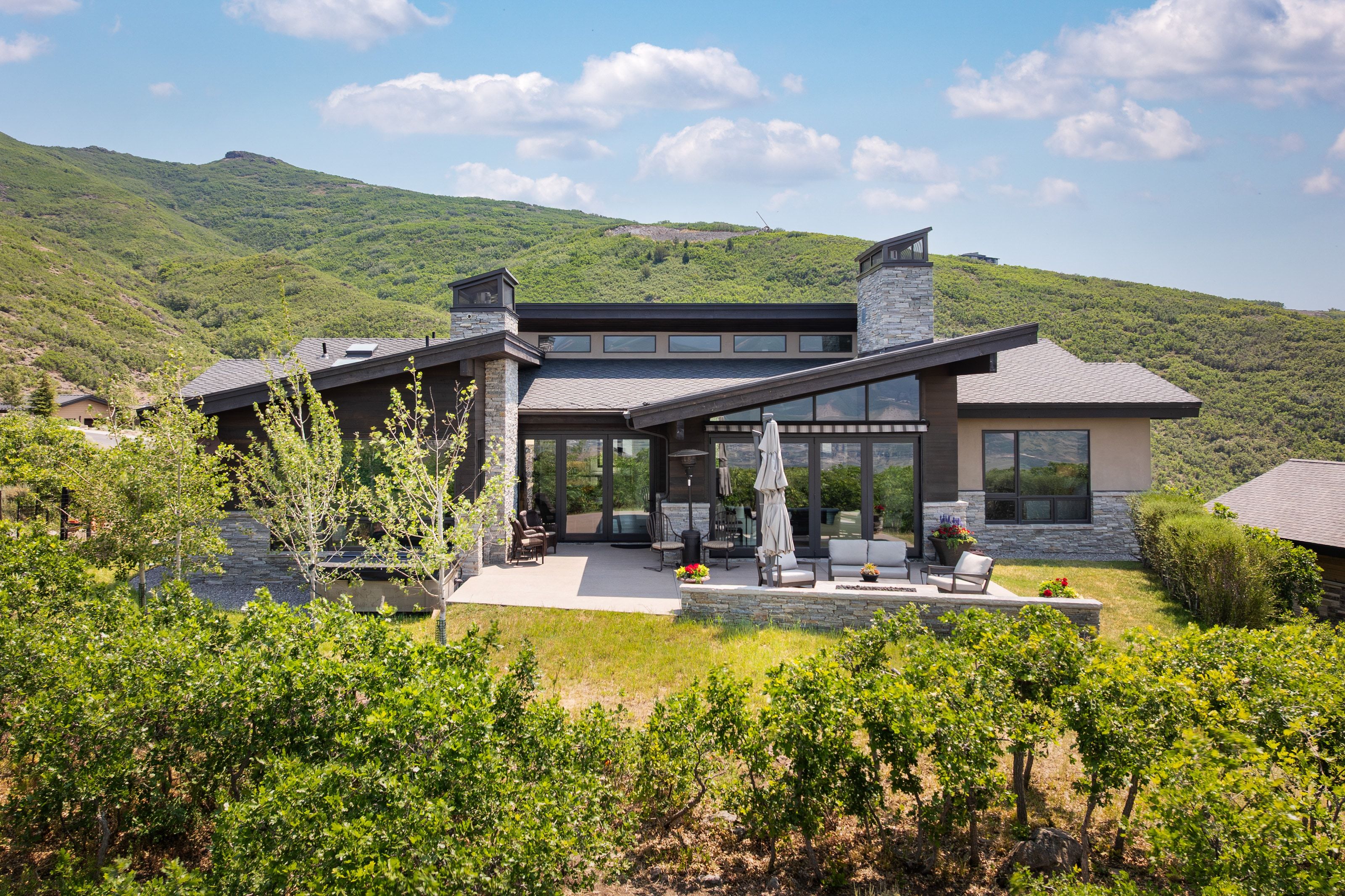 Modern mountain residence featuring a multi-level patio, stone accent walls, and a prominent chimney
