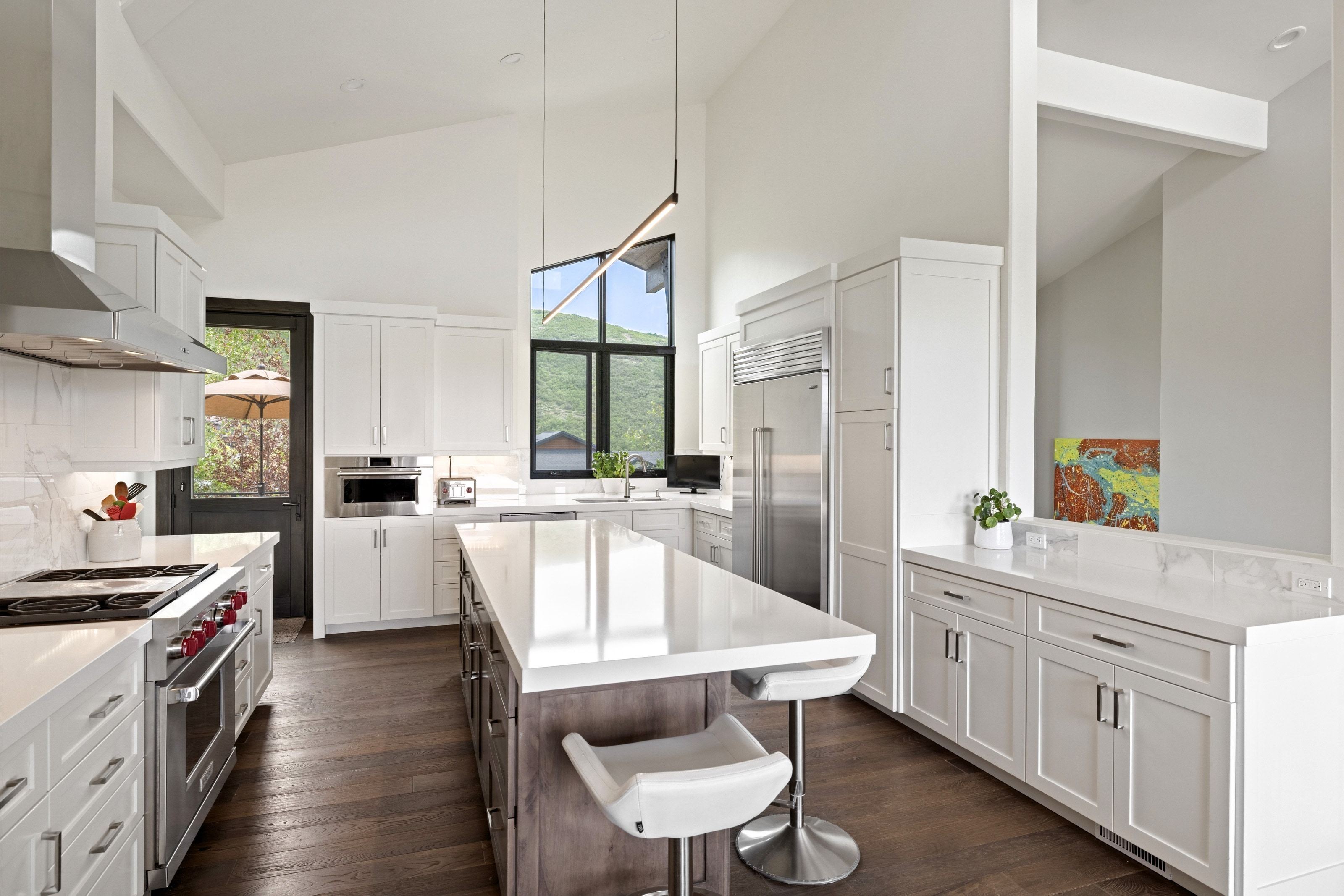 Open-concept kitchen featuring a large central island, white cabinetry, dark wood-finish flooring, stainless steel appliances, and high vaulted ceilings