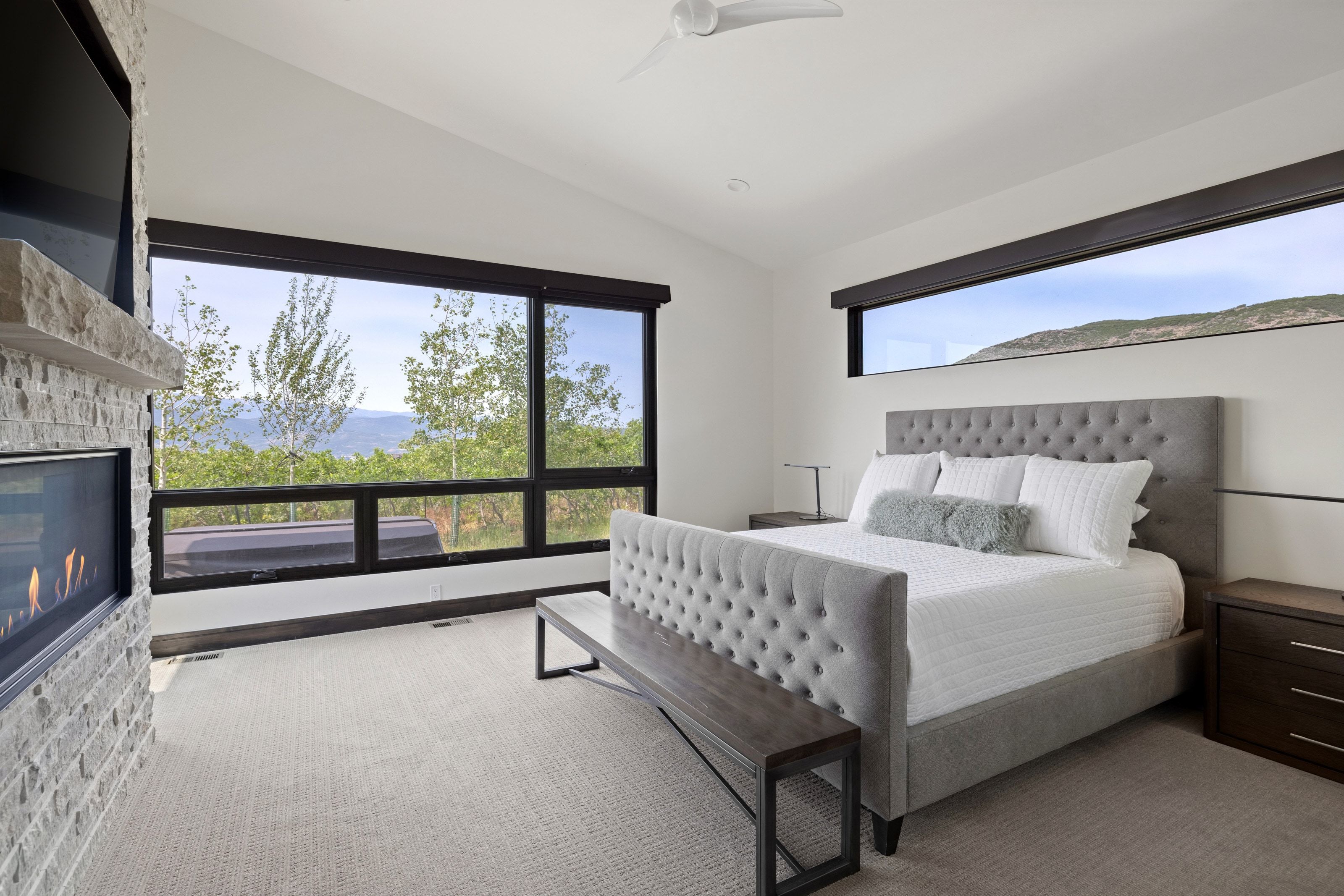 Spacious bedroom featuring large picture windows, a linear fireplace with stone surround and stone mantel, a vaulted ceiling, and recessed lighting
