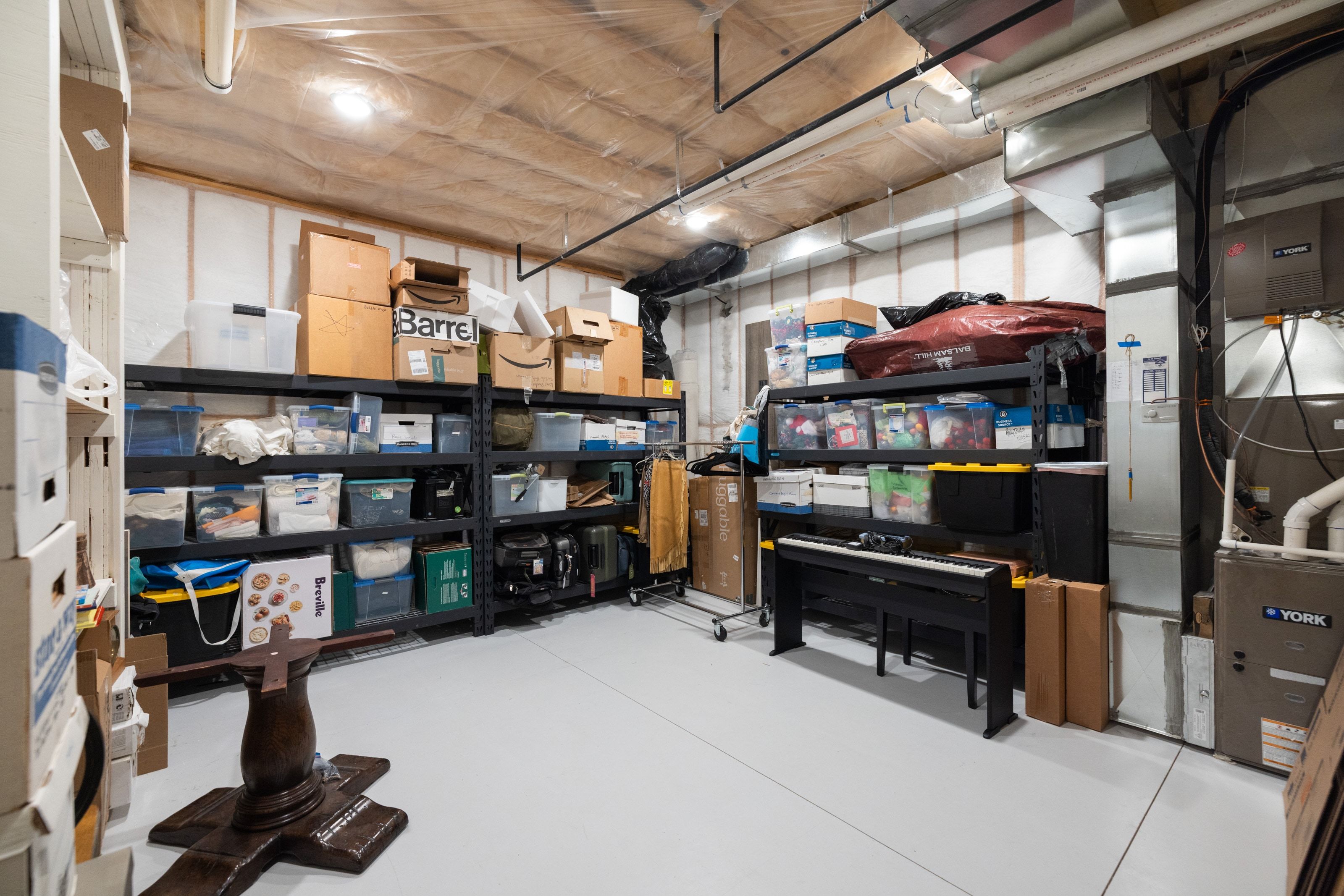 Finished basement storage room featuring painted concrete flooring, exposed ceiling joists, and utility access