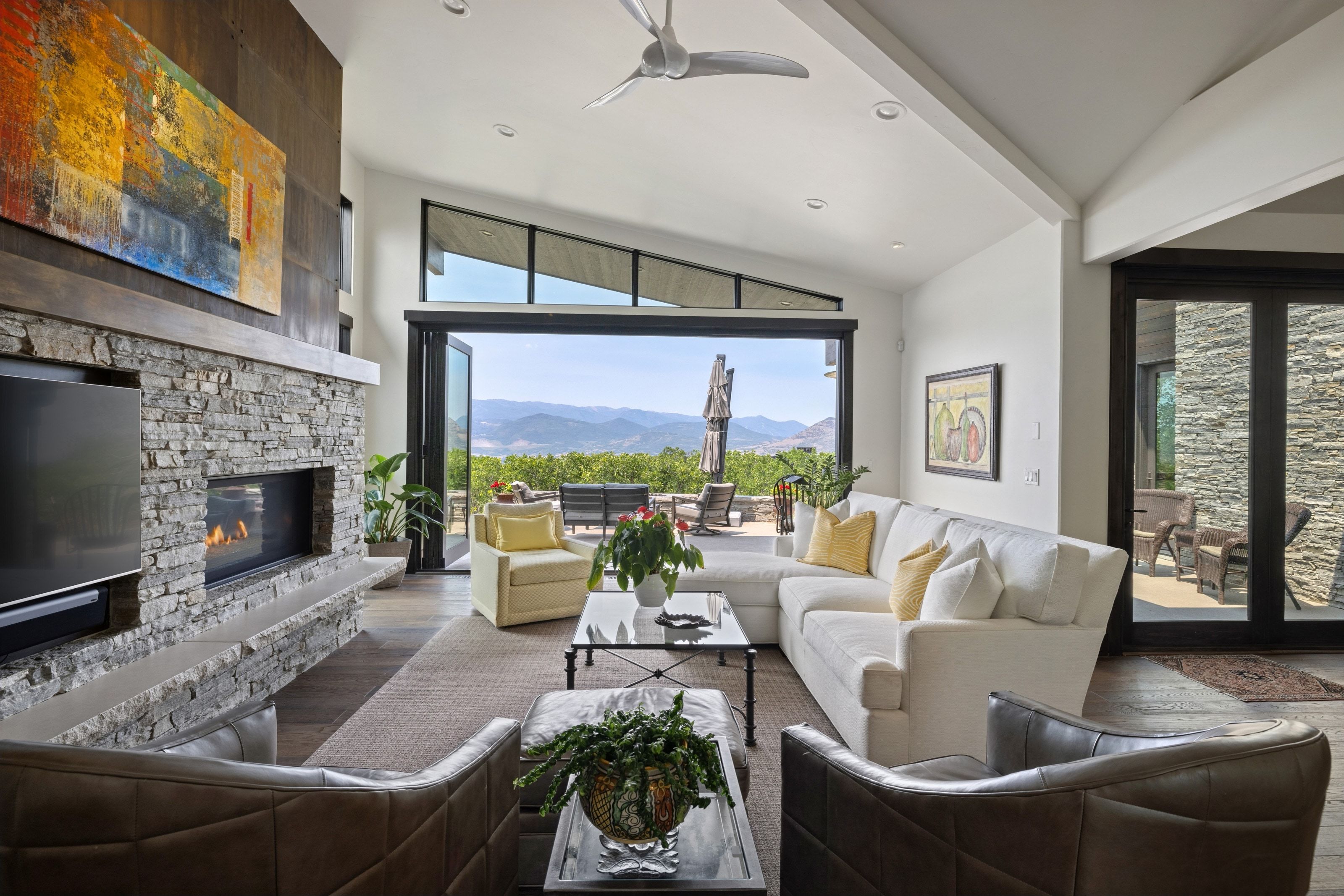 Spacious living area featuring a stacked stone fireplace with a built-in media center, vaulted ceilings, and large bi-fold glass doors opening to the exterior