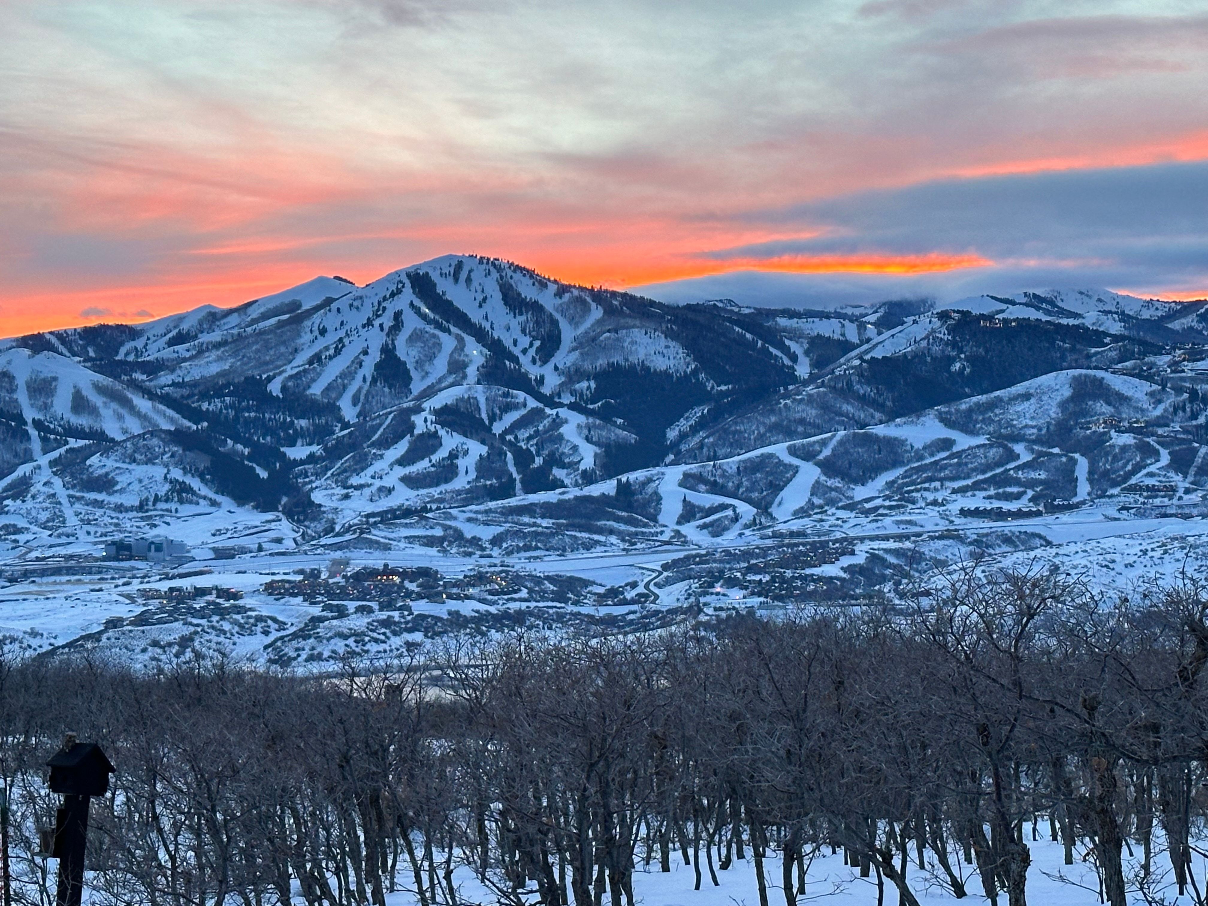 Expansive mountain landscape featuring snow-covered peaks, ski slopes, and a vibrant sunset sky