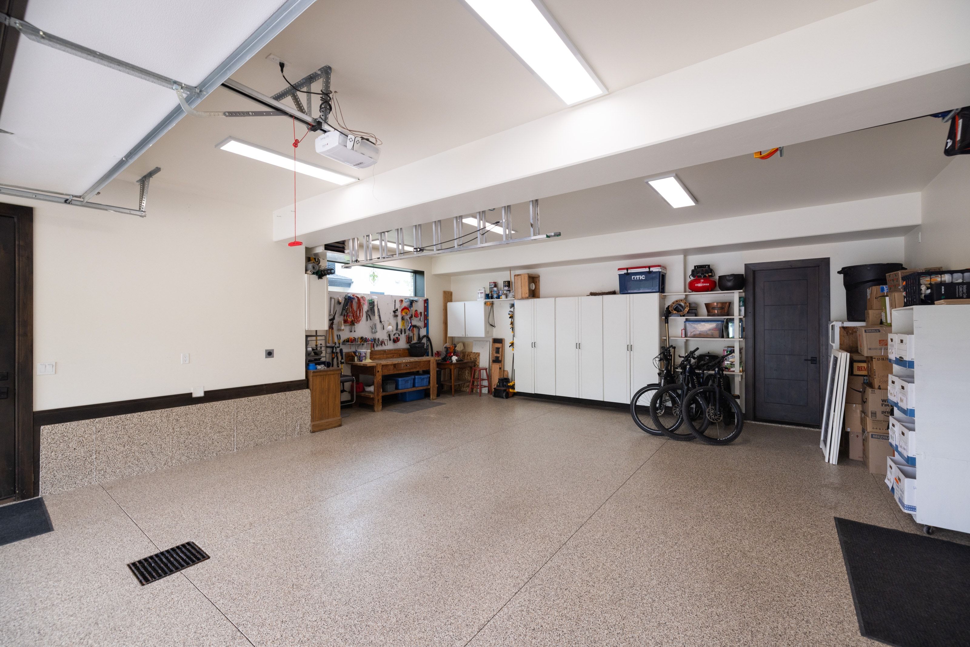 Spacious garage featuring a durable epoxy flooring system, overhead lighting, and extensive built-in cabinetry for organized storage