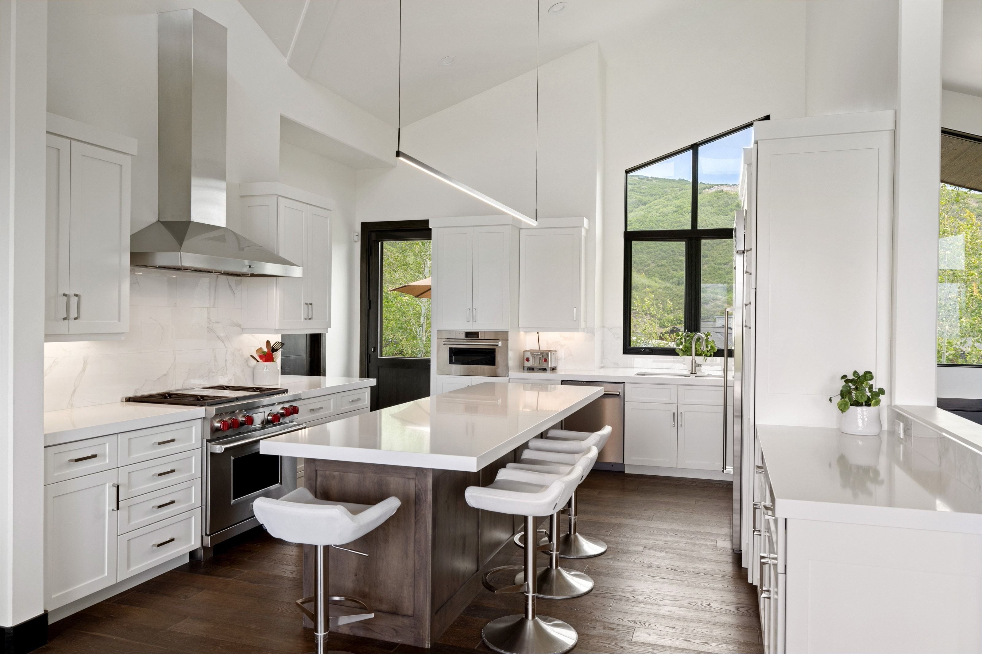 Vaulted kitchen featuring white cabinetry, a large center island with seating, dark wood-finish flooring, and a stainless steel appliance suite