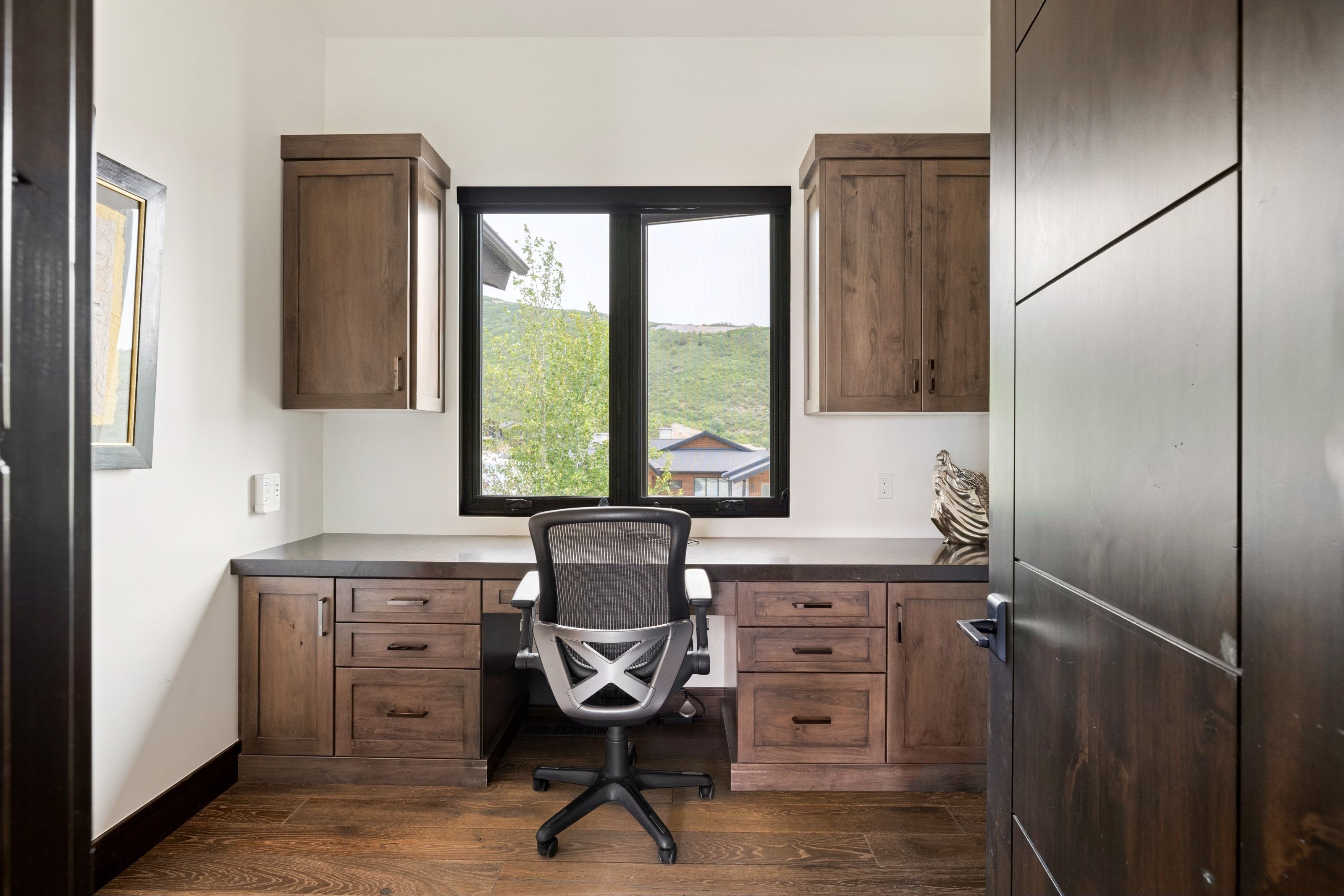 Dedicated workspace featuring custom wood cabinetry, integrated desk, and coordinating wood-finish flooring