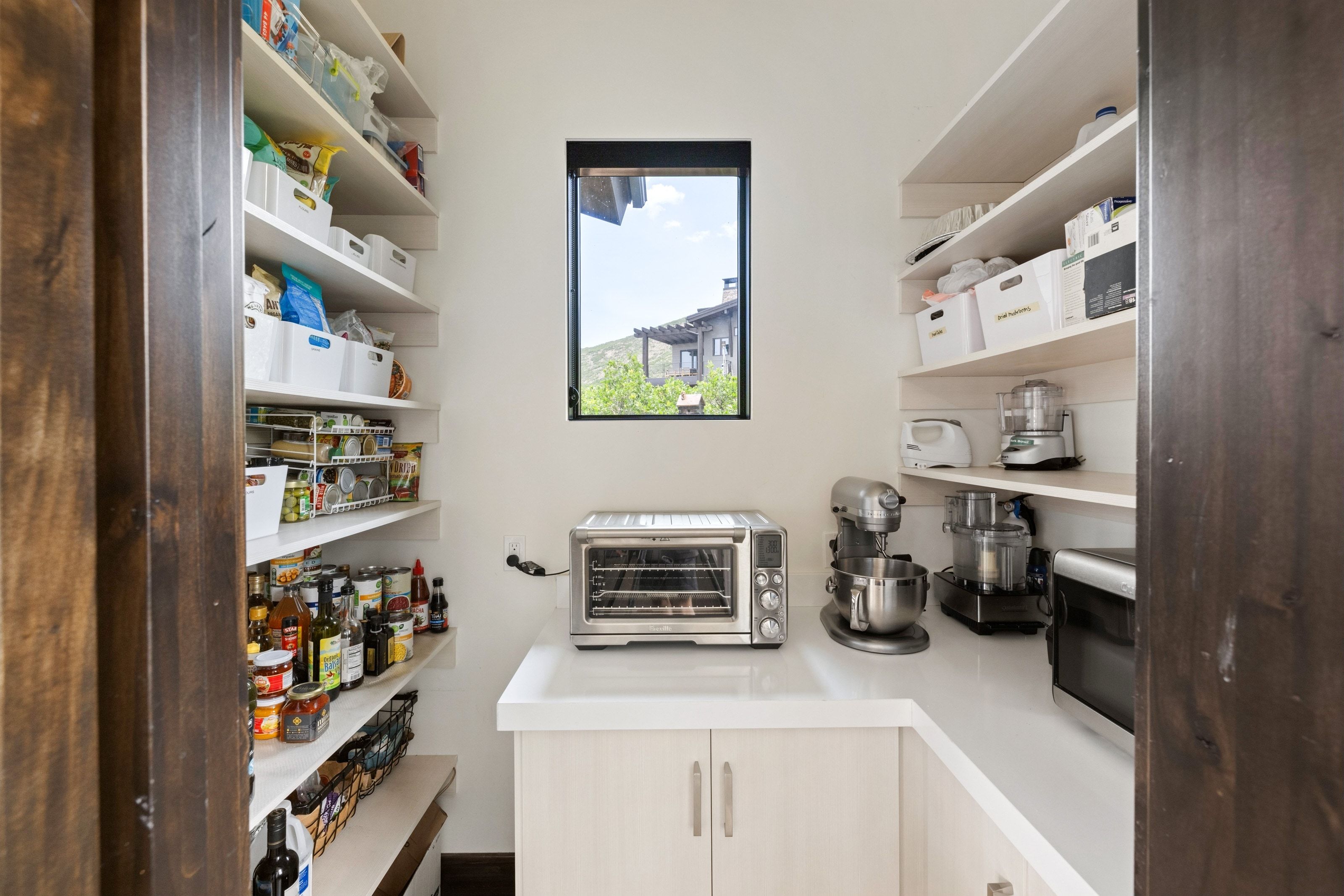 Walk-in pantry featuring extensive built-in shelving, white countertops, and light-toned cabinetry with modern hardware