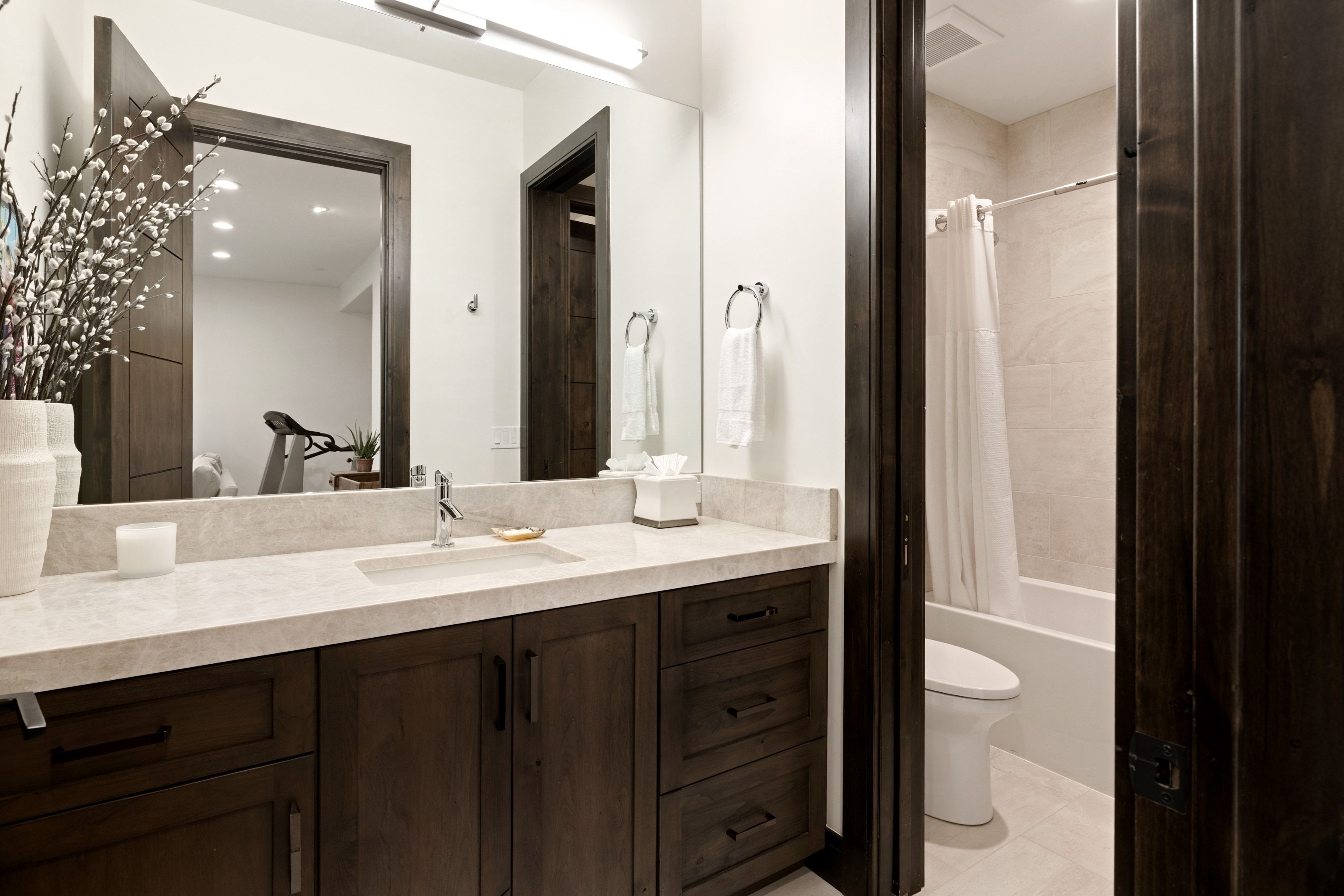 Bathroom featuring a large vanity with a light-toned countertop, integrated rectangular sink, dark wood-finish cabinetry with black hardware, and a framed mirror with overhead lighting