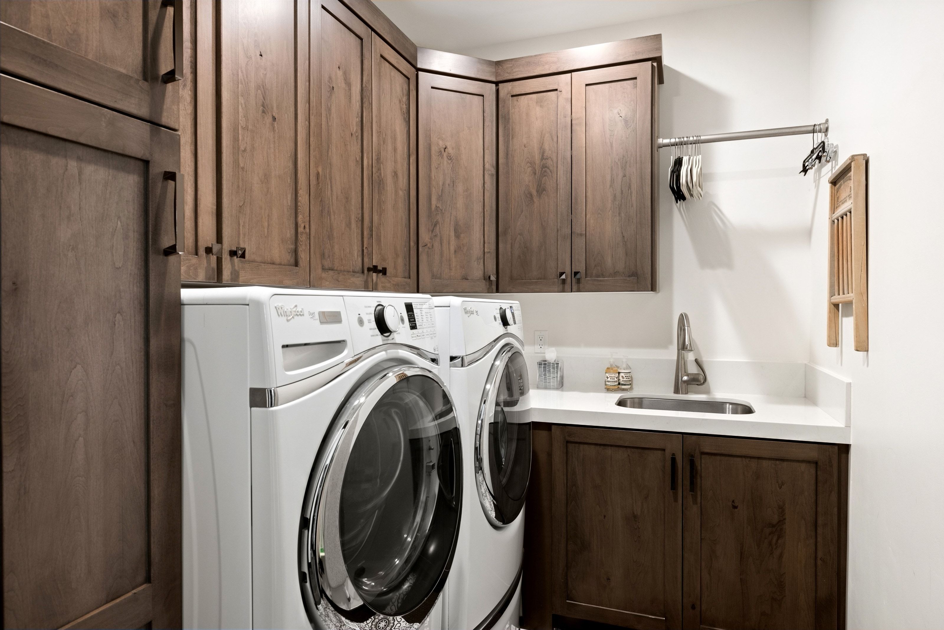 Dedicated laundry area featuring a front-load washer and dryer, extensive wood-finish cabinetry, a white countertop, and an undermount sink with a gooseneck faucet