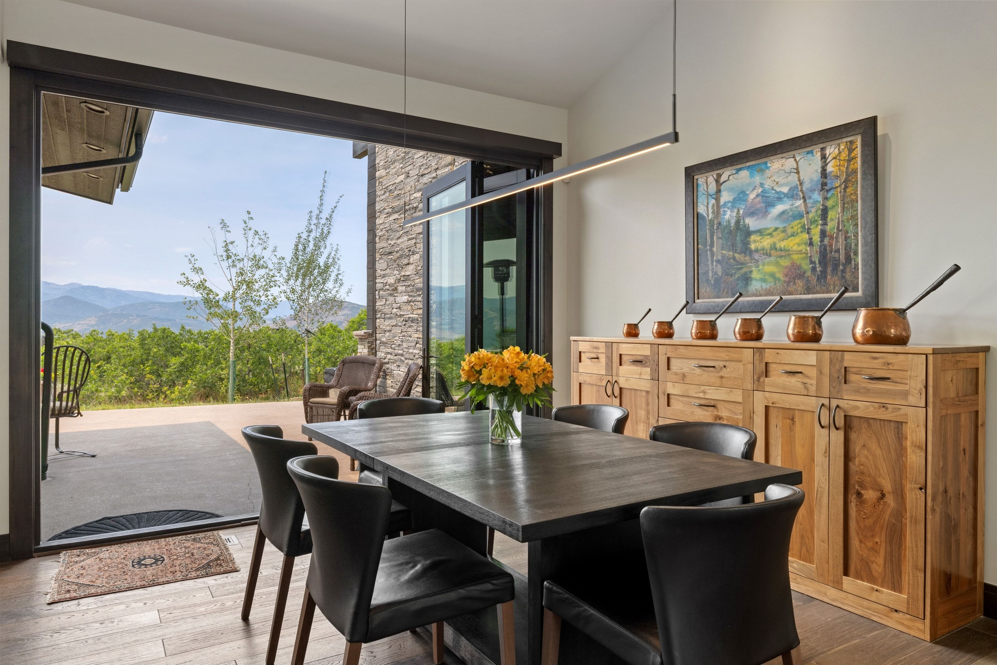 Open-concept dining area featuring wood-finish flooring, a linear pendant light fixture, and a full-height glass sliding door opening to an outdoor patio
