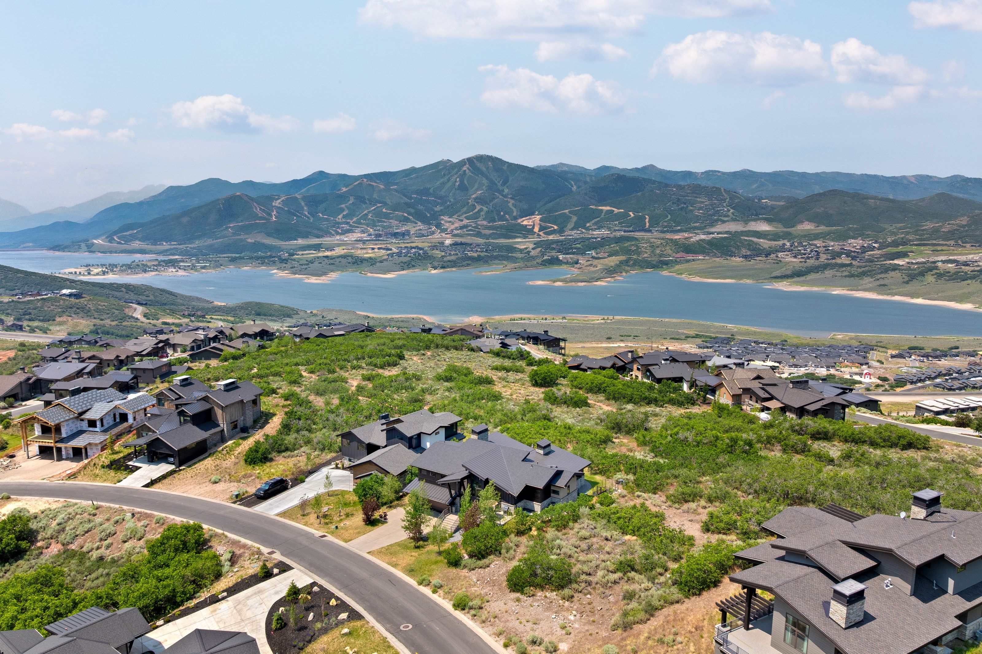 Expansive landscape featuring an elevated residential area with modern homes, a tranquil lake, and distant mountains