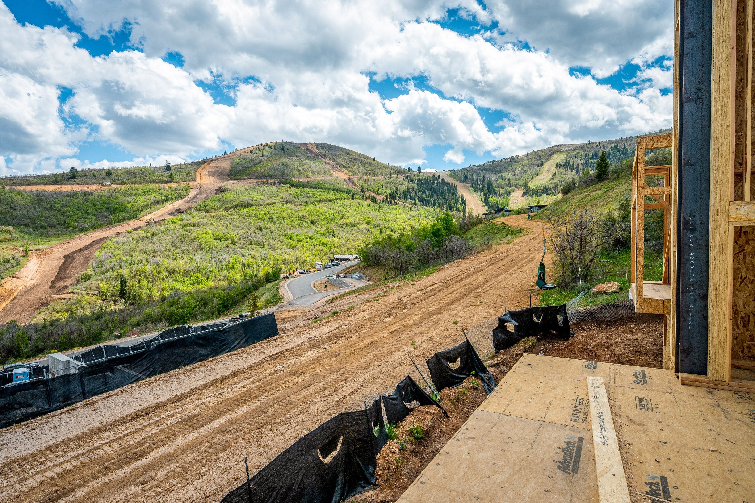 Framed construction with visible exterior sheathing and structural lumber, set against a backdrop of rolling green hills with visible ski runs