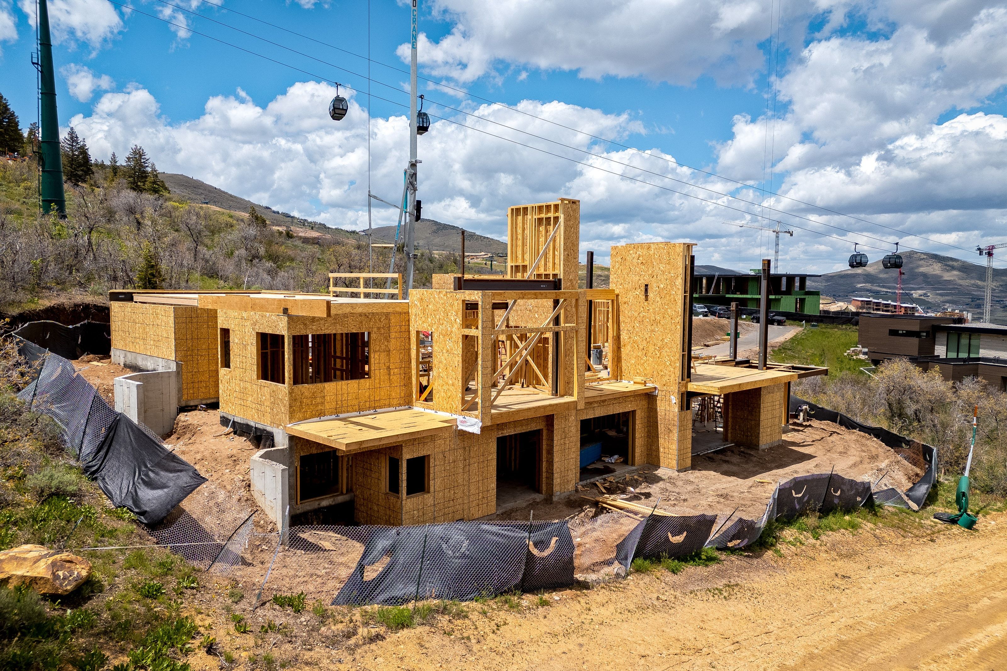 New construction framing in progress with structural sheathing, multiple window openings, and concrete foundation elements