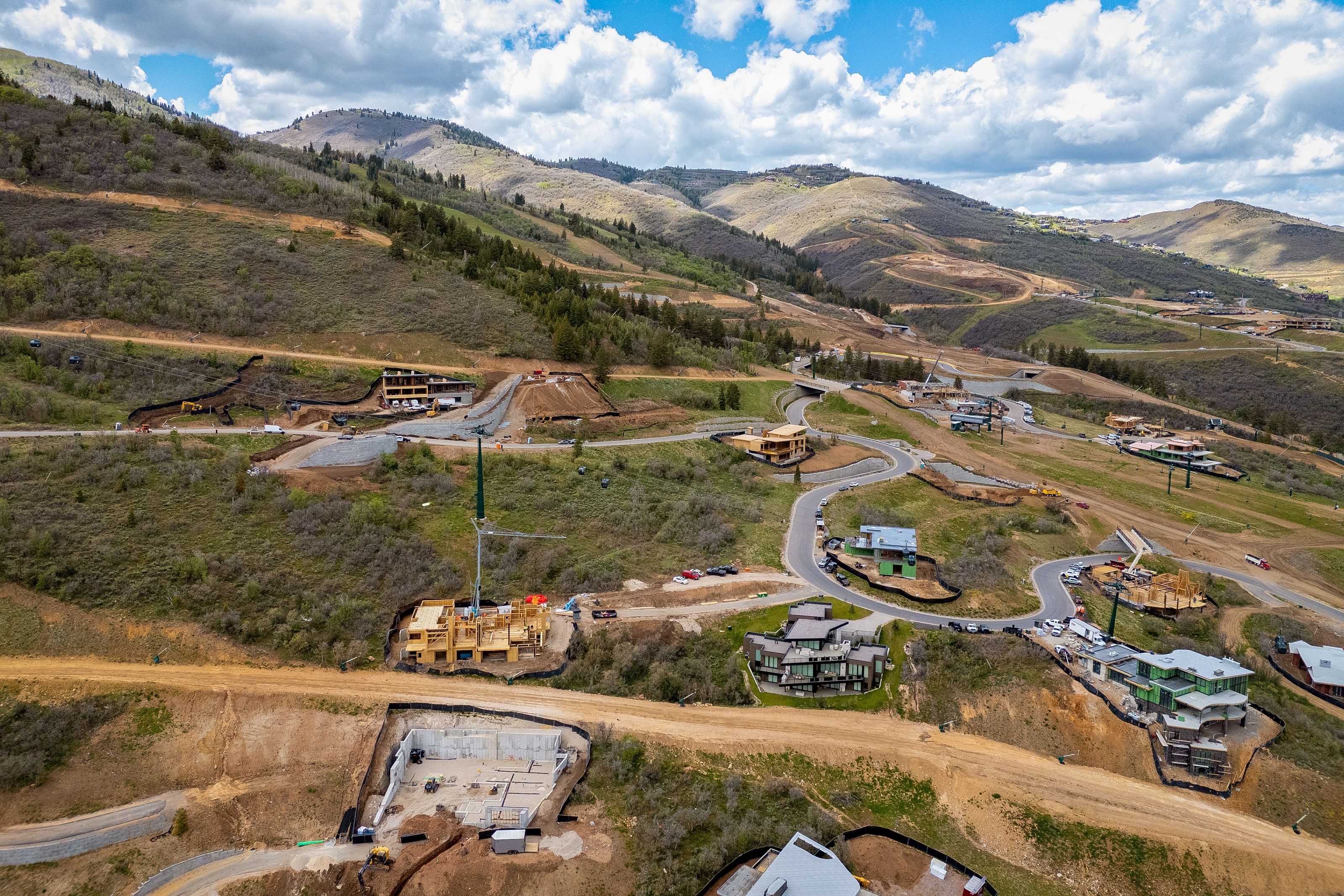 Terraced hillside properties with varying stages of construction, featuring a winding road system and mountainous terrain