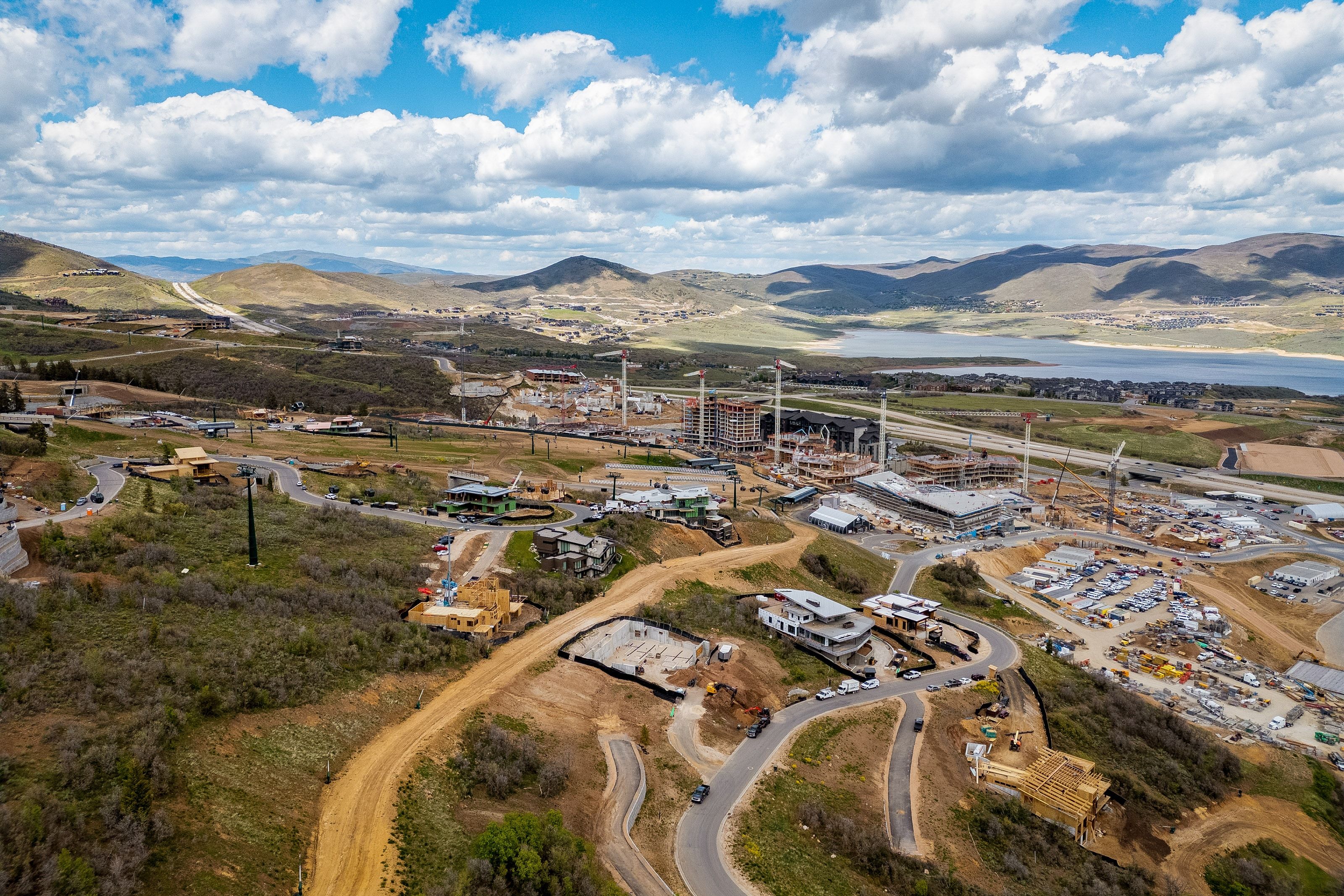 Aerial panorama showcasing hillside development with ongoing construction, surrounding mountainous terrain, and a prominent body of water in the distance