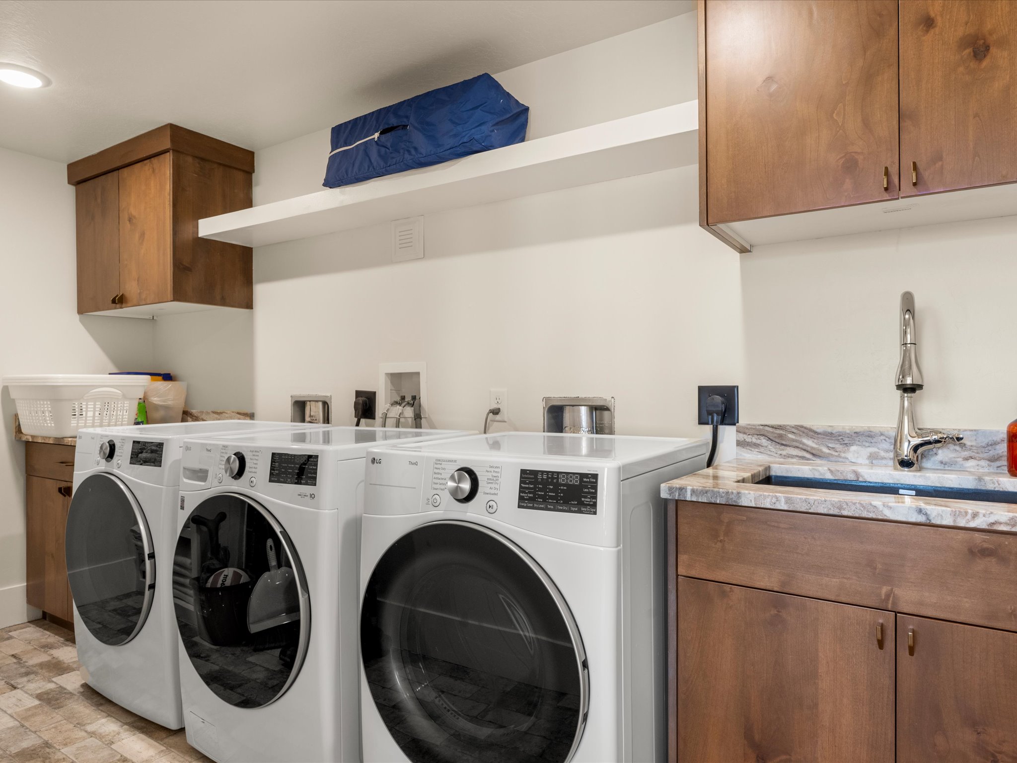 Laundry area featuring a built-in utility sink, stone countertop, wood cabinetry, and a floating shelf