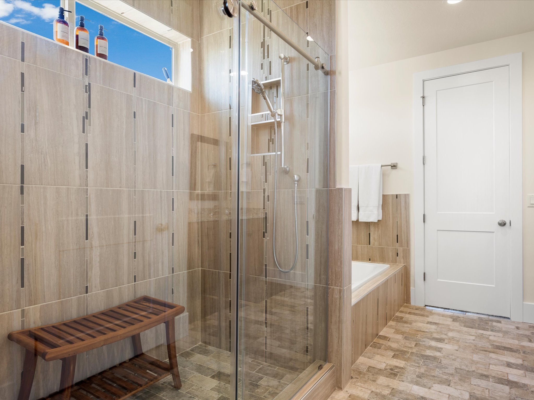 Spacious shower enclosure with glass surround, integrated shelving, and wood-look tile walls