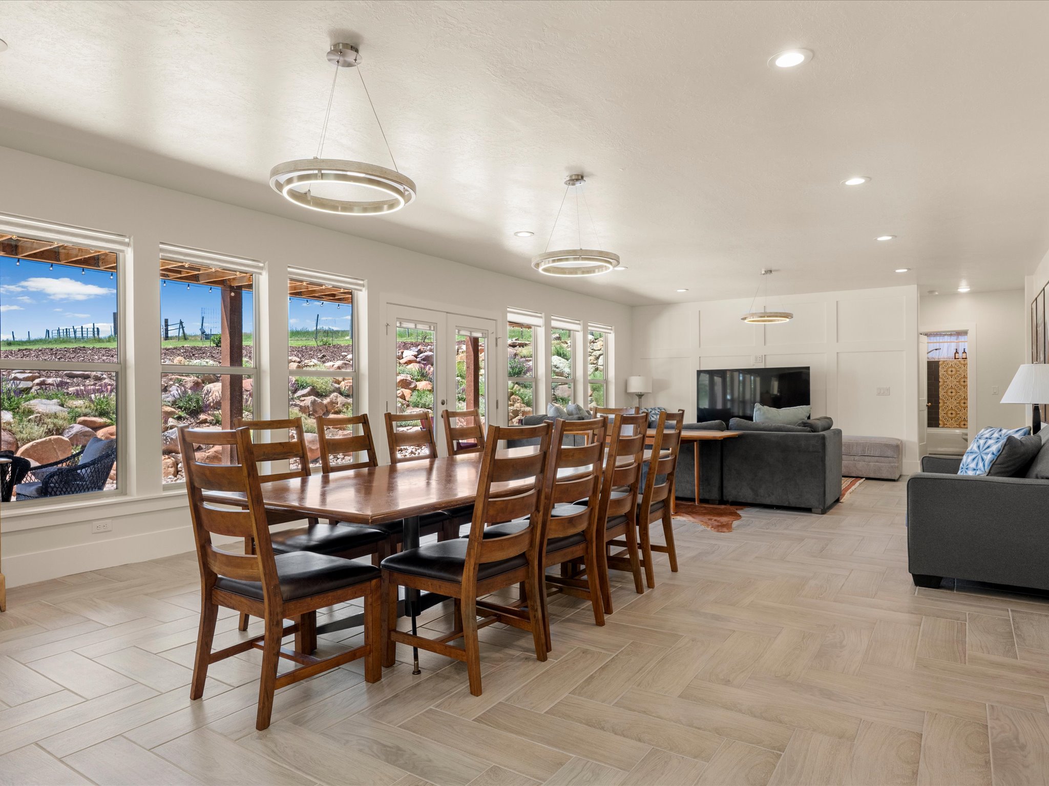 Open-concept living area featuring a large dining table, herringbone tile flooring, multiple windows, and recessed lighting