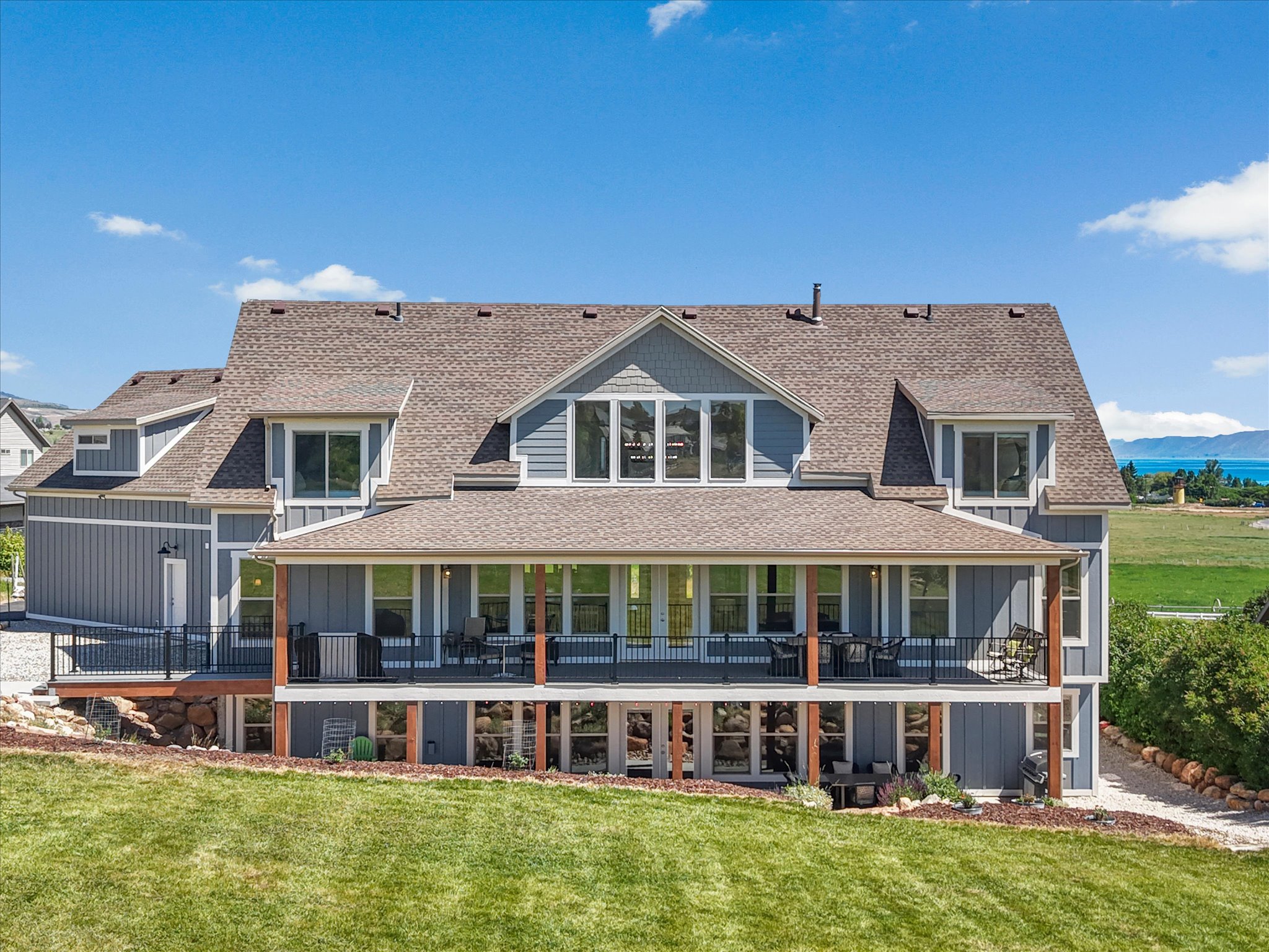 Multi-level residential exterior featuring blue siding, a shingle roof, and a covered patio with wooden columns