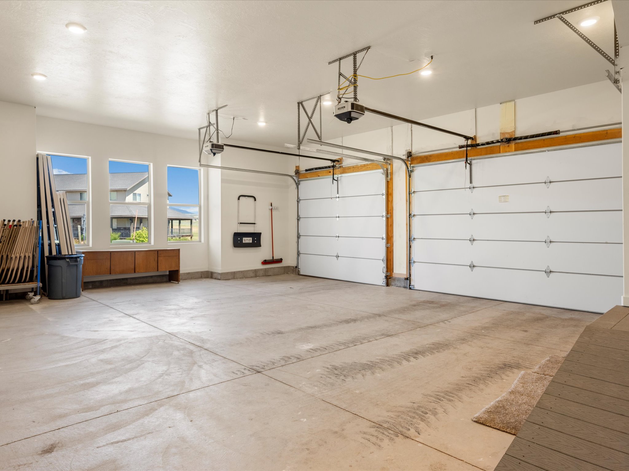 Spacious garage featuring two overhead garage doors, ample concrete flooring, recessed ceiling lighting, and multiple windows providing natural light
