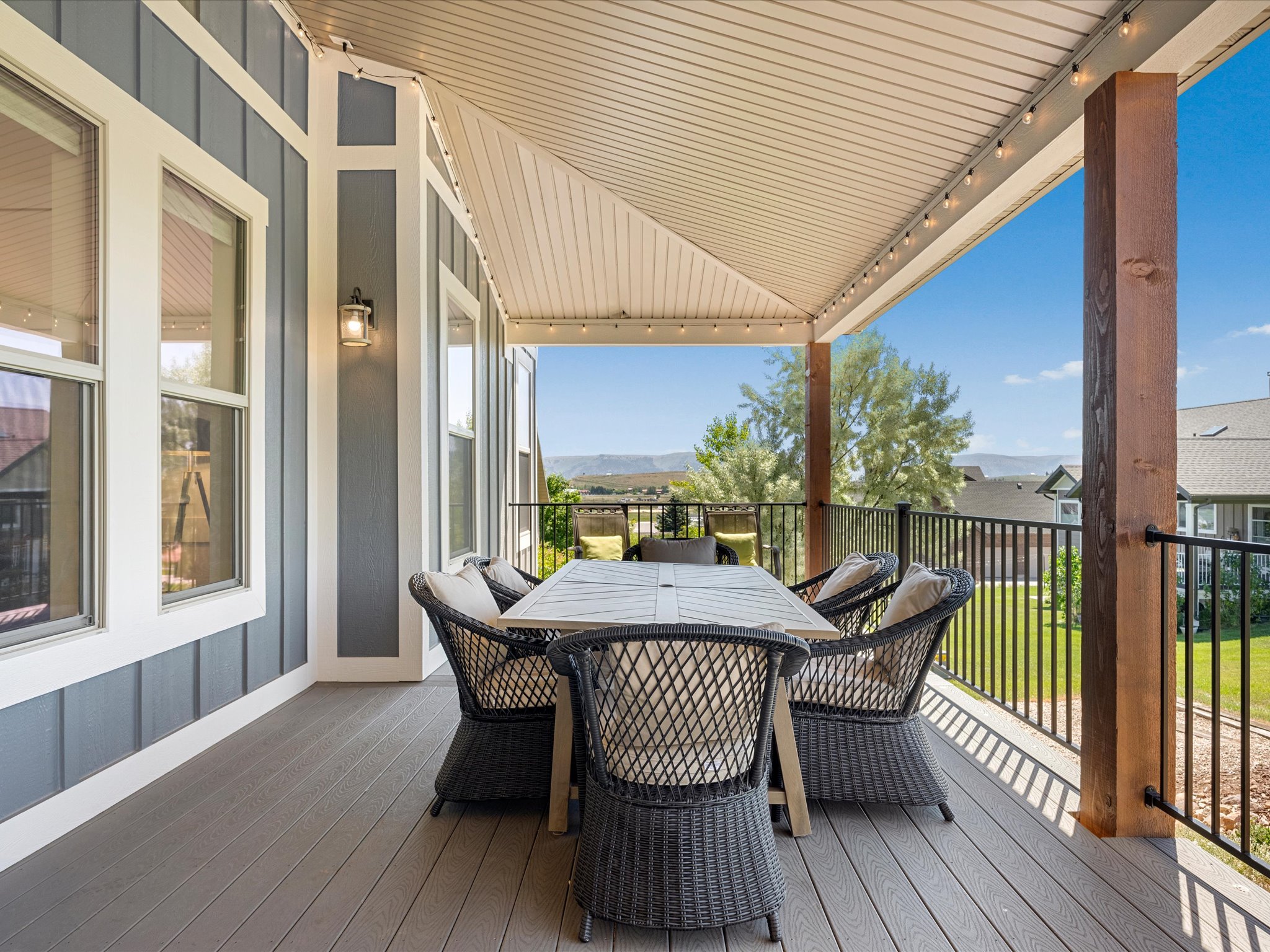 Covered outdoor patio featuring composite decking, vertical siding with white trim, and a black metal railing