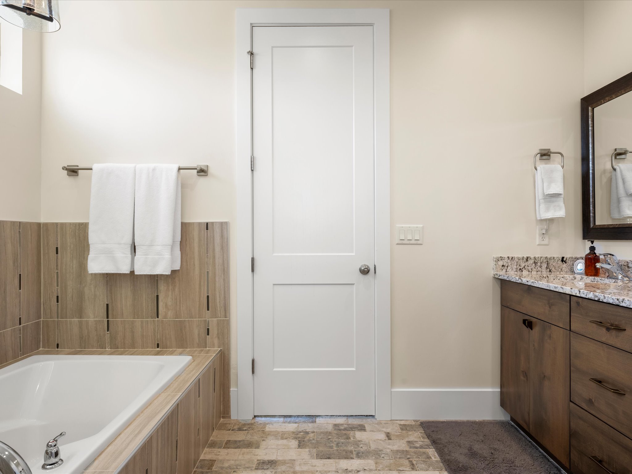 Modern bathroom featuring a built-in tub with tile surround, a wood-finish vanity with a stone countertop, a framed mirror, and tile flooring