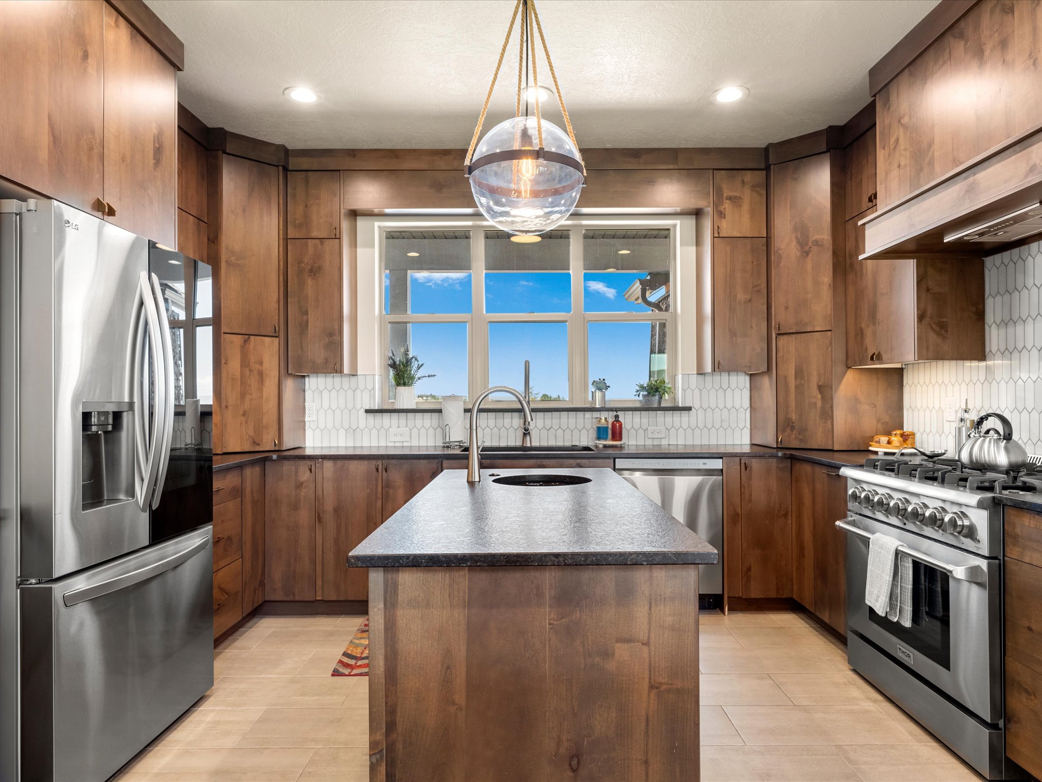 Modern kitchen featuring rich wood cabinetry, stainless steel appliances, a central island with a sink, and a stylish picket tile backsplash