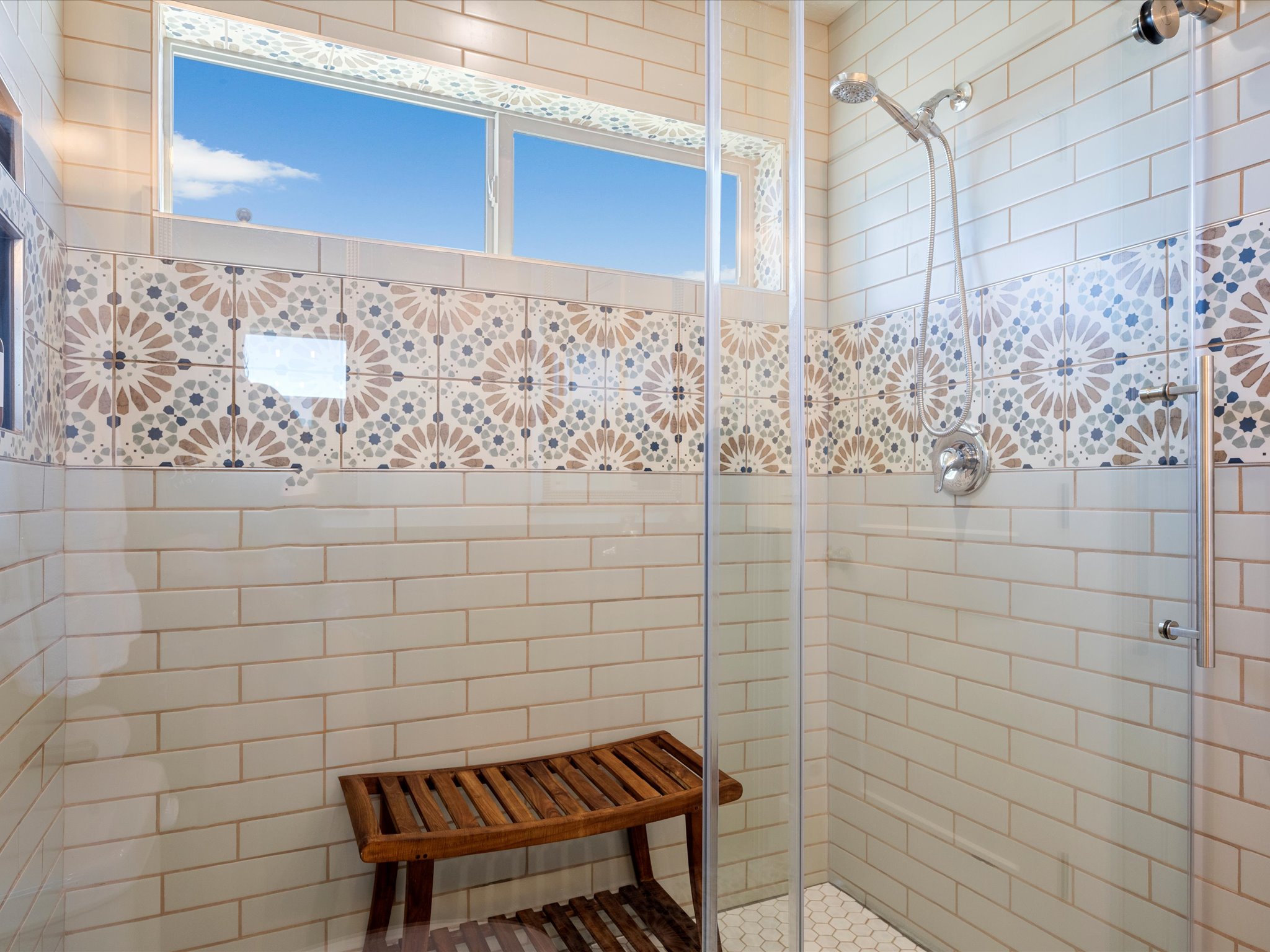 Shower enclosure featuring patterned accent tile, subway tile surround, clear glass paneling, a rain showerhead, and hexagon tile flooring