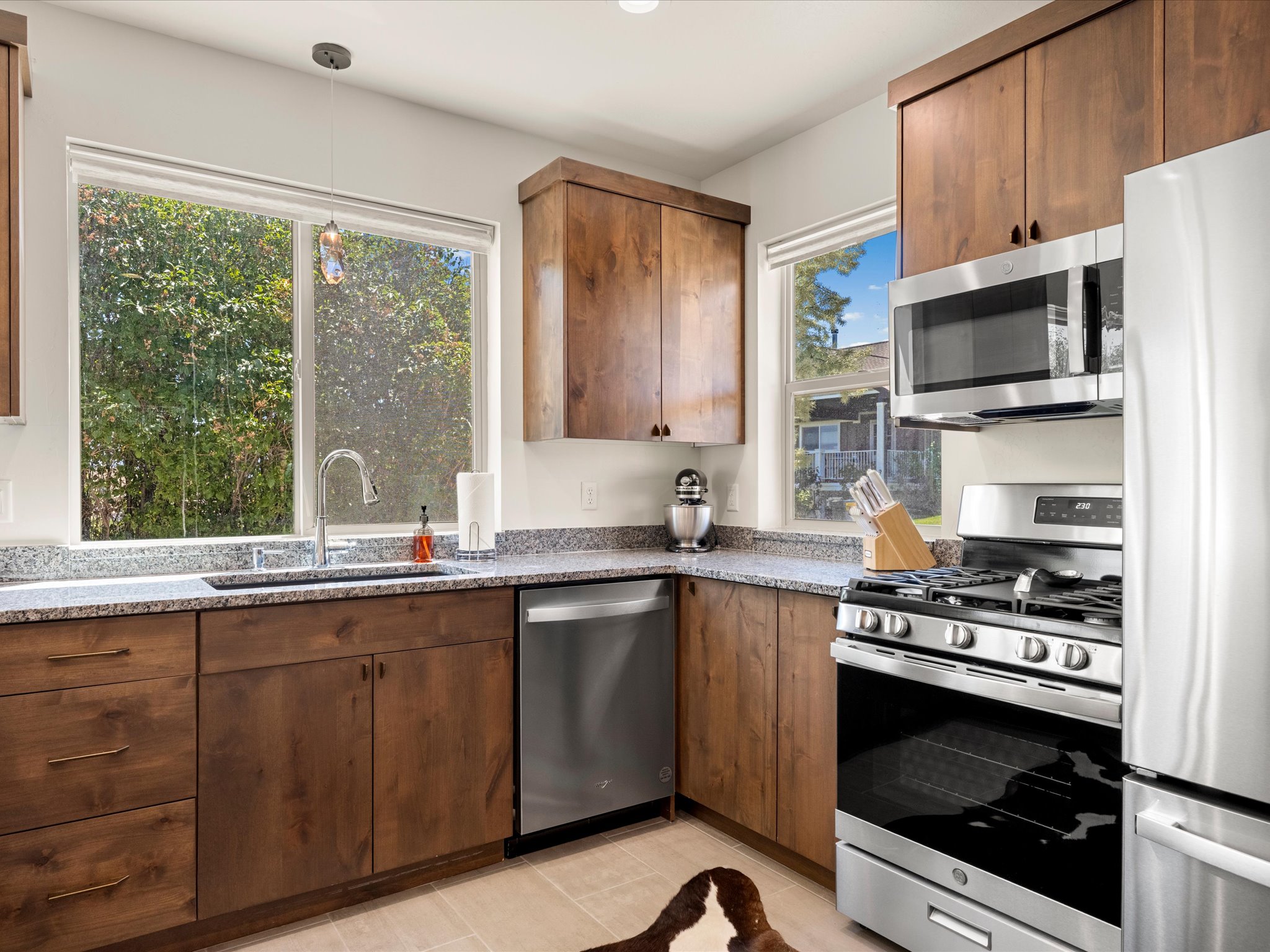 Kitchen featuring a large window over the sink, wood cabinetry, stone countertops, and stainless steel appliances including a gas range, microwave, dishwasher, and refrigerator