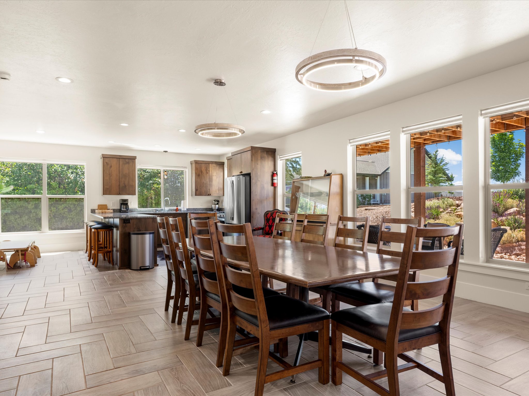 Spacious open-concept living area featuring light-toned tile flooring in a herringbone pattern, recessed lighting, and contemporary circular chandeliers