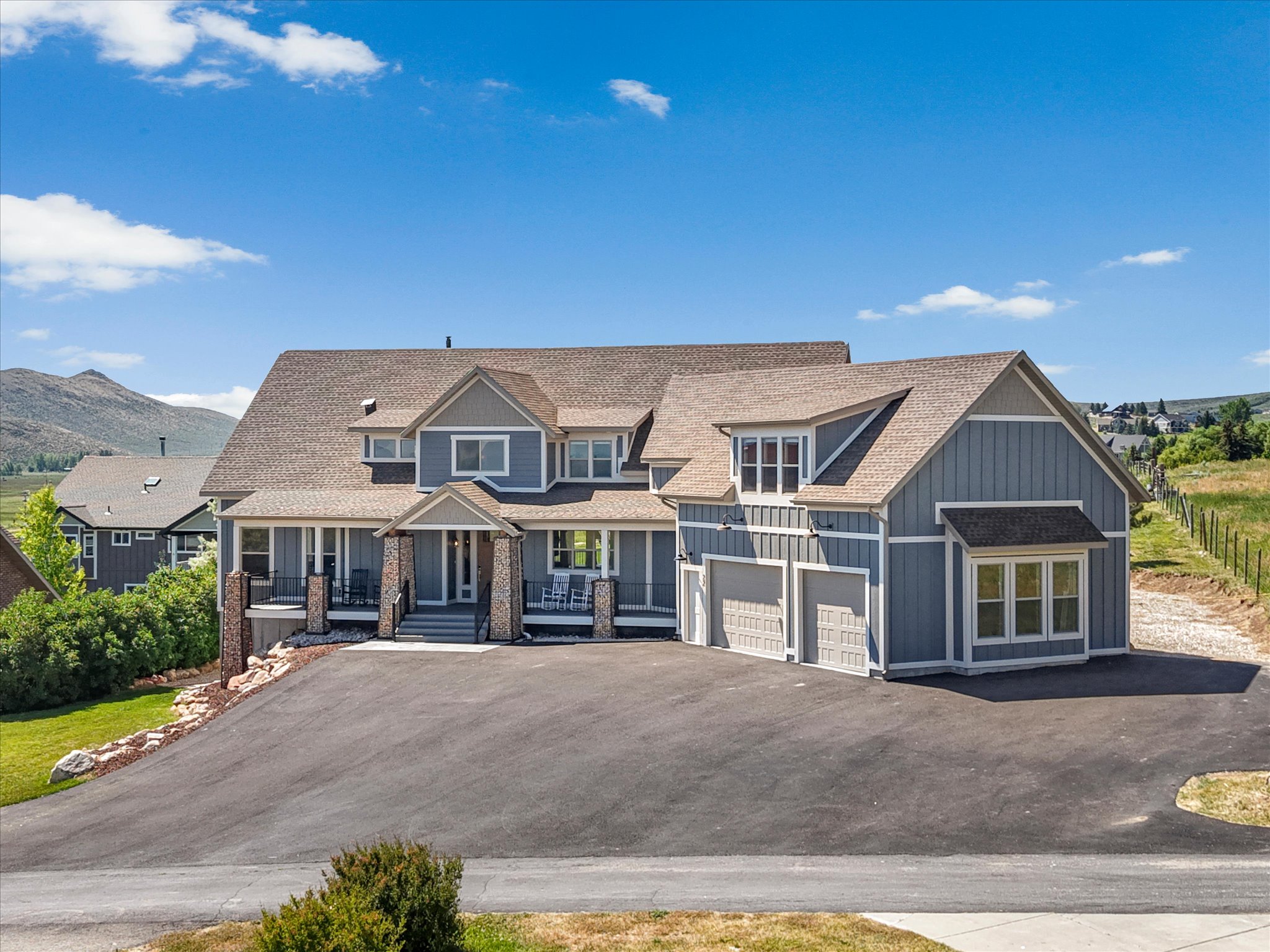 Expansive residence featuring a multi-gable roofline, two levels of covered front porches, a garage, and a wide paved driveway