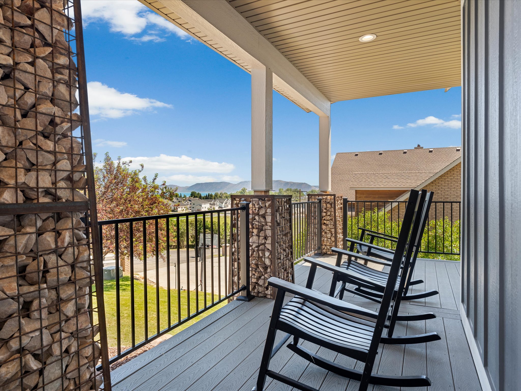 Covered outdoor deck featuring stone-filled gabion wall accents, black metal railing, and composite decking