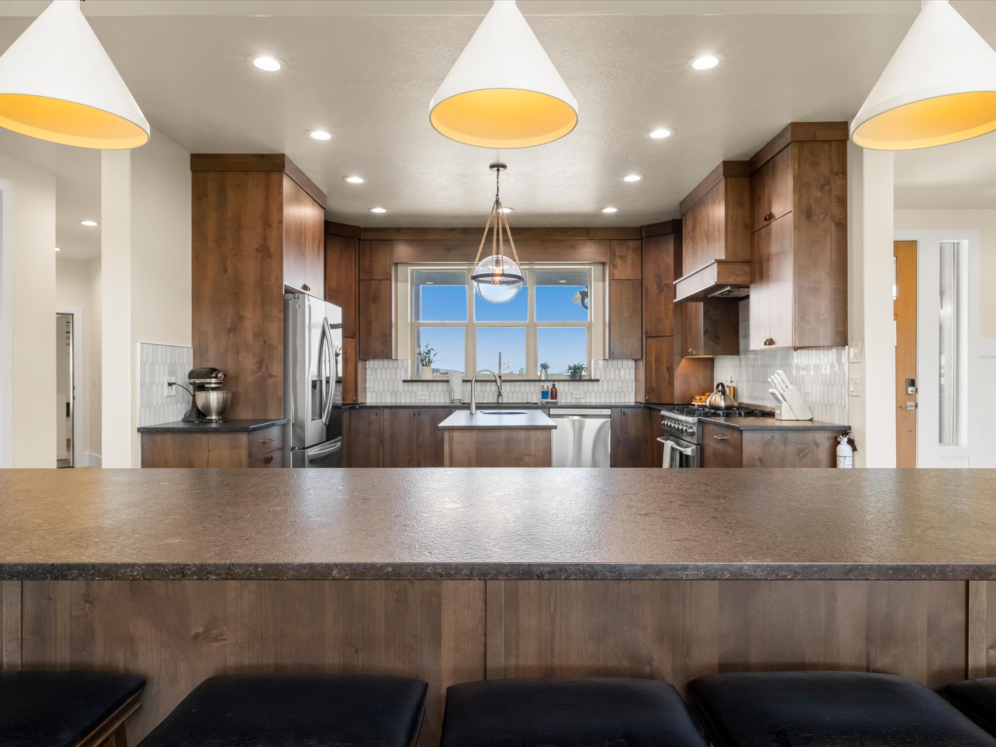Kitchen featuring dark wood cabinetry, stainless steel appliances, a center island with a sink, a tiled backsplash, and recessed lighting