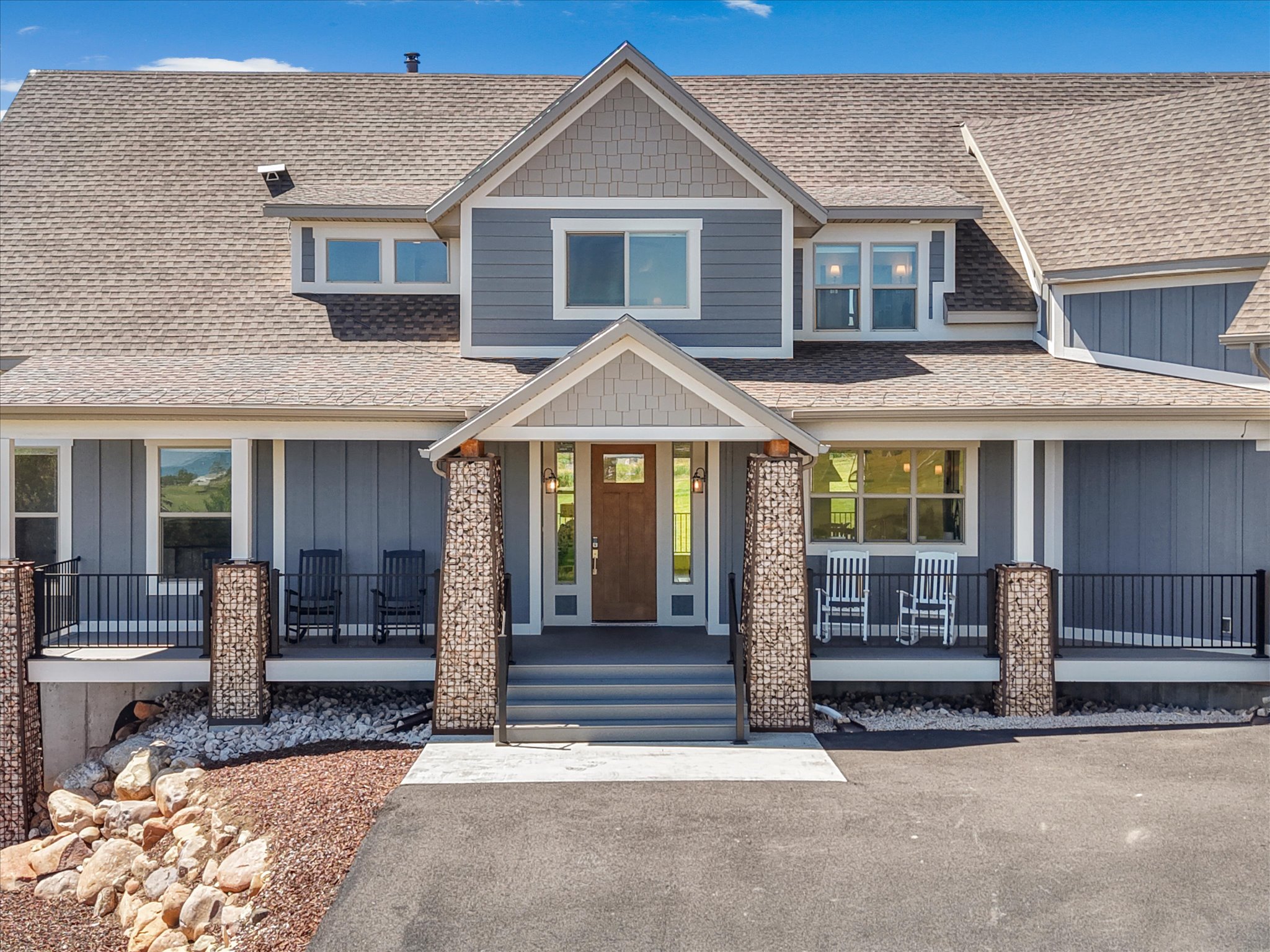 Modern farmhouse exterior featuring gray siding, a prominent gable, a covered porch with gabion columns, a solid wood entry door, and a shingled roof