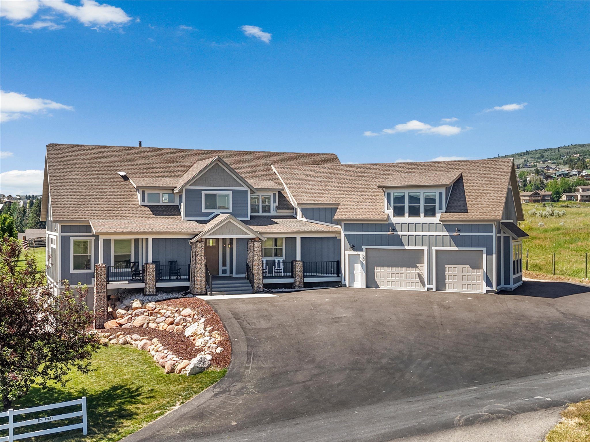 Expansive residence featuring a multi-gable roof, a covered front porch with stone-clad columns, a paved driveway, a garage, and landscaped rock gardens