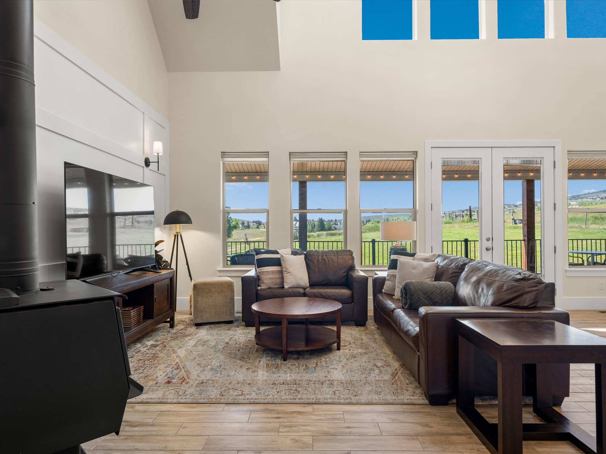 Vaulted living area featuring a prominent wood-burning stove, wall-mounted television, and wood-finish tile flooring