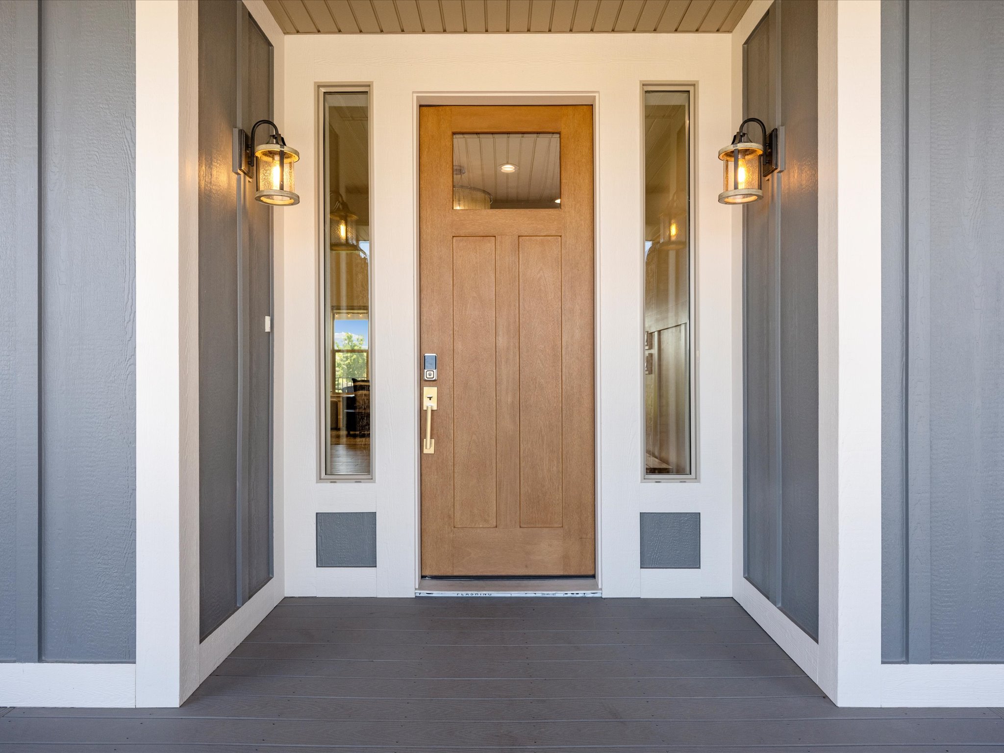 Inviting front entryway featuring a natural wood-finish door with glass pane, flanked by vertical sidelight windows and two exterior sconces with seeded glass